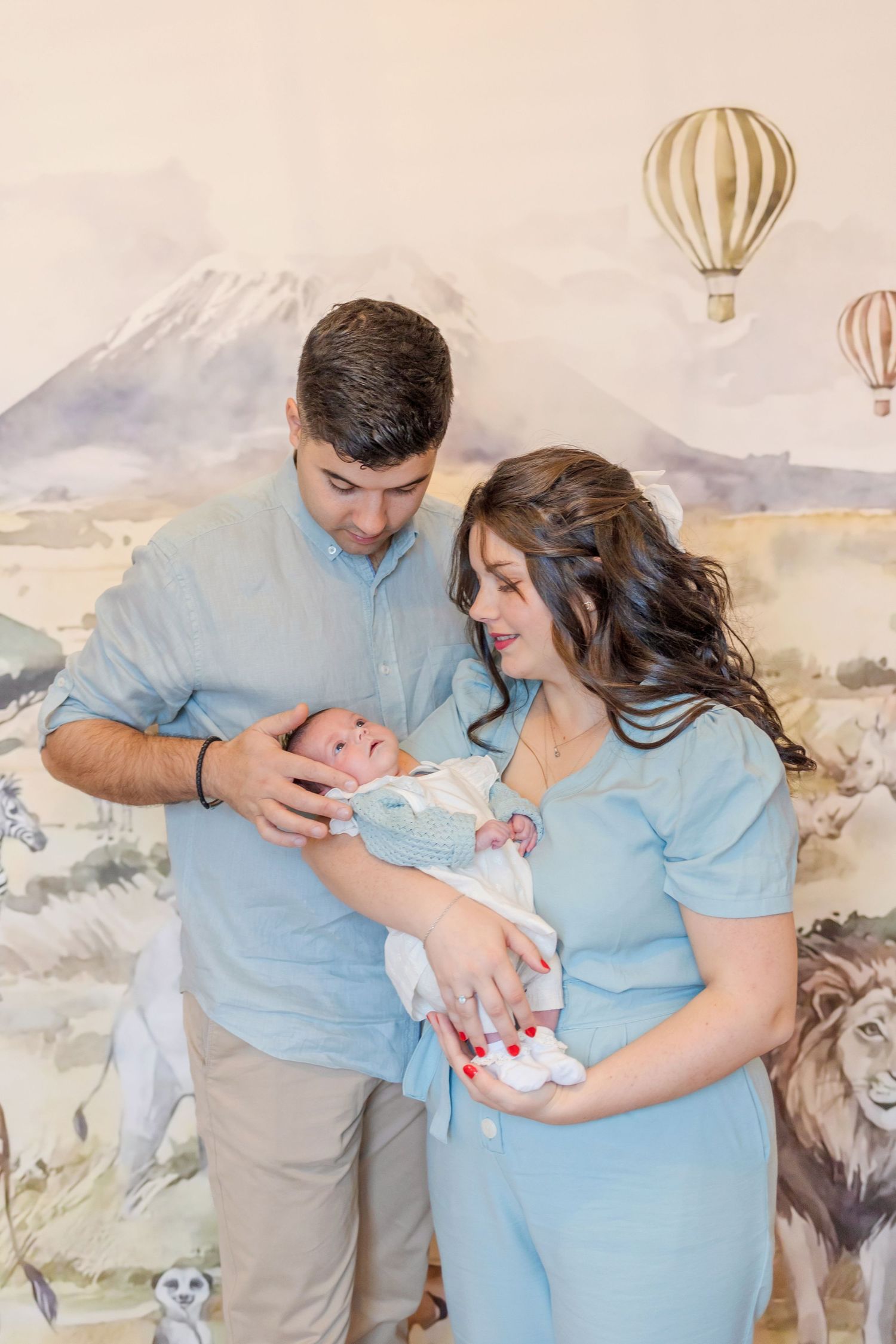 A touching family portrait in coordinating blue outfits against a whimsical safari wall mural.