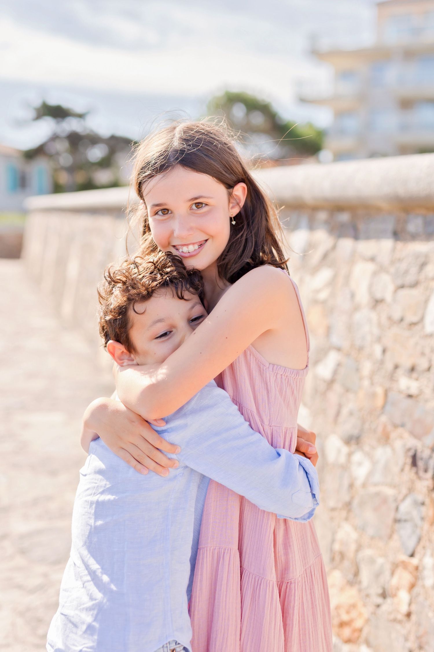 Sweet embrace between siblings on sunny coastal walkway.
