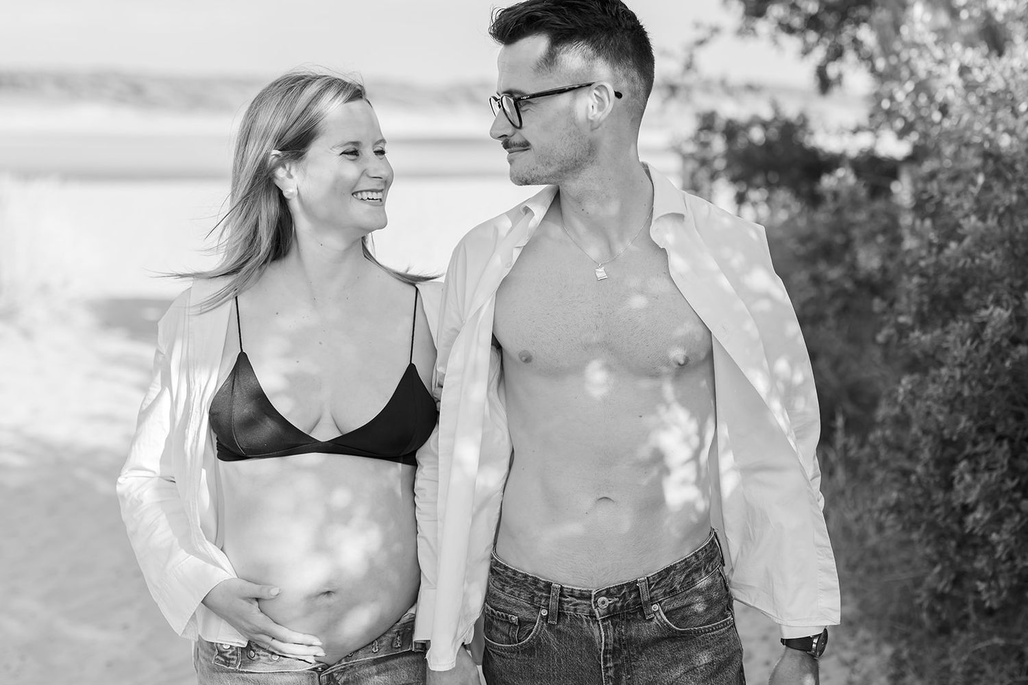 A series of black and white romantic engagement photos showing a couple embracing and walking together in nature.