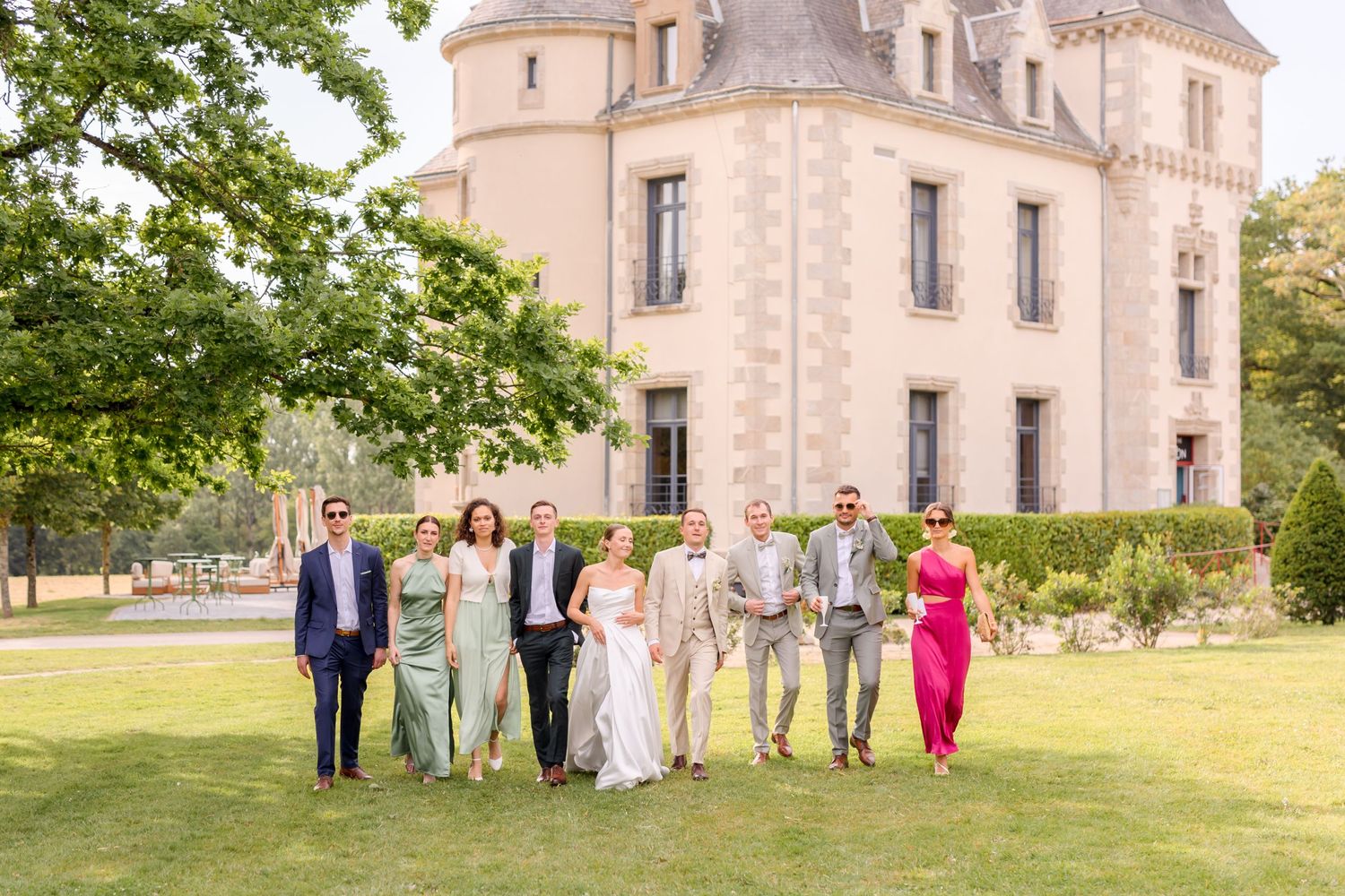 Wedding group poses in front of majestic chateau with stone architecture and landscaped grounds.
