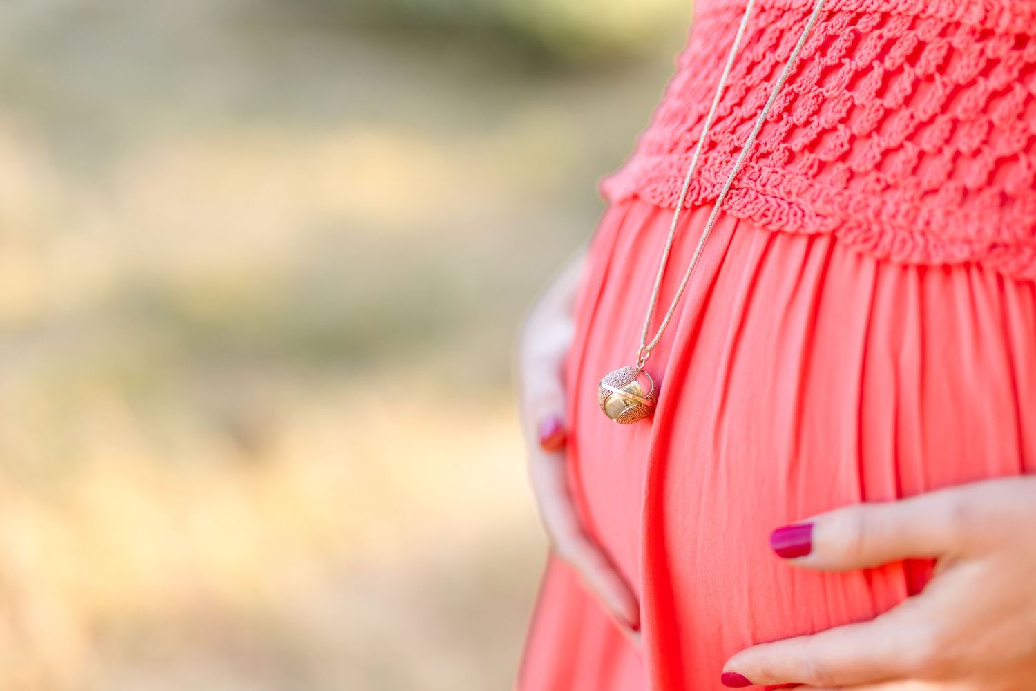 Close-up view of a coral crochet detailed sundress in warm sunlight.