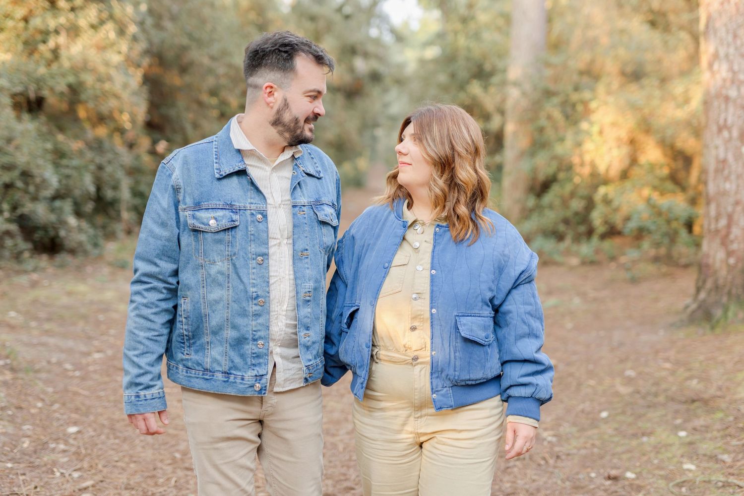 Couple in matching denim jackets walking together on an autumn path in golden sunlight.