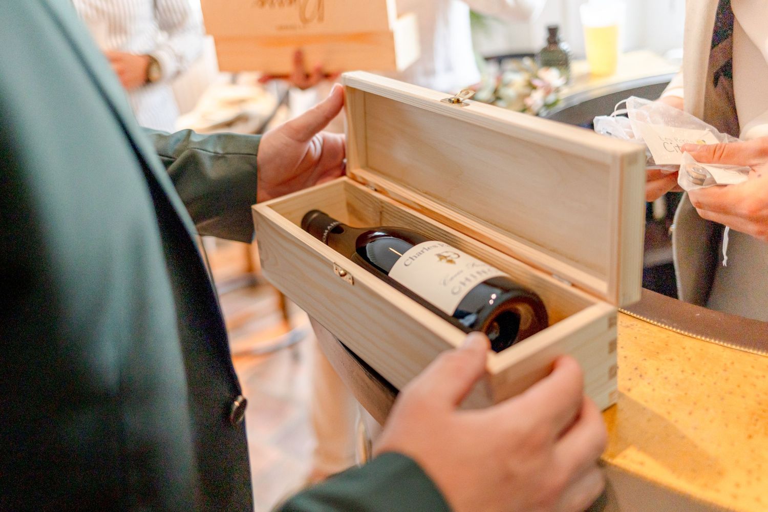 Hands opening a wooden box containing wine bottles at an event.