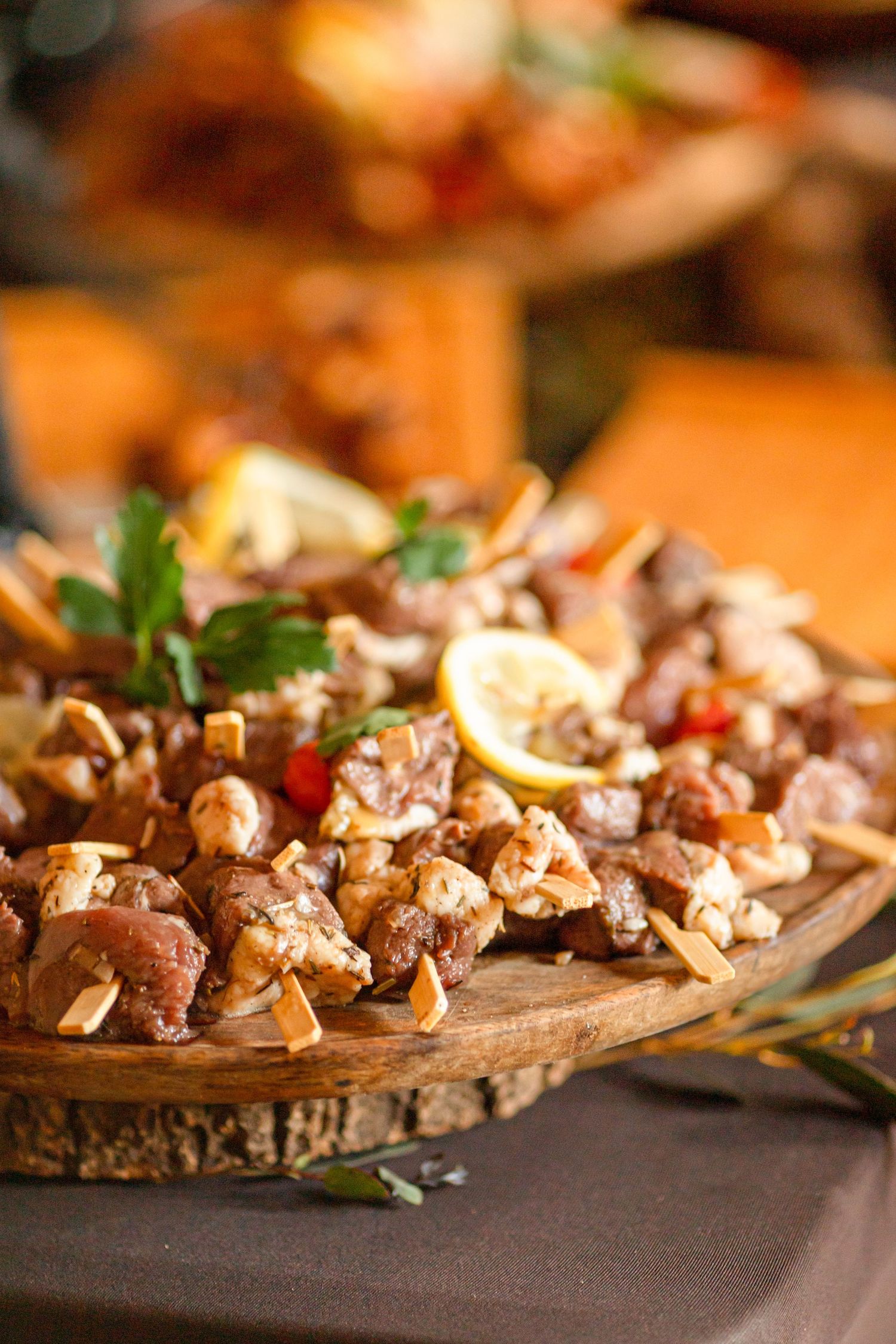 Rustic wooden platter filled with grilled meat skewers garnished with lemon slices and herbs.