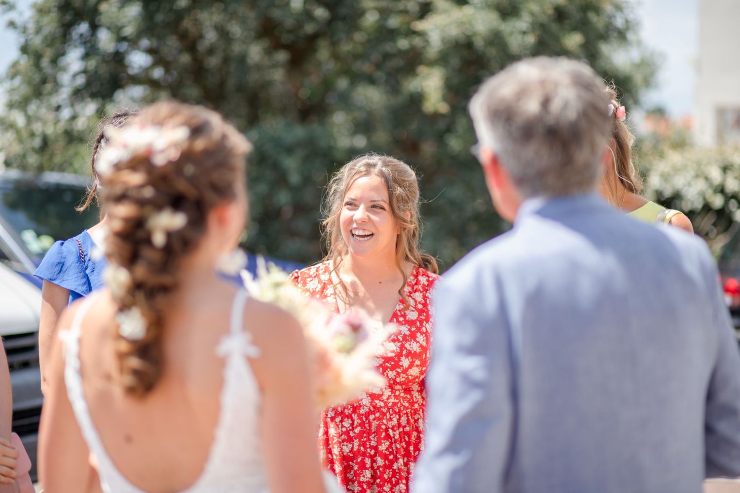 Wedding party members gathered outdoors on a sunny day wearing blue suits and red dresses.