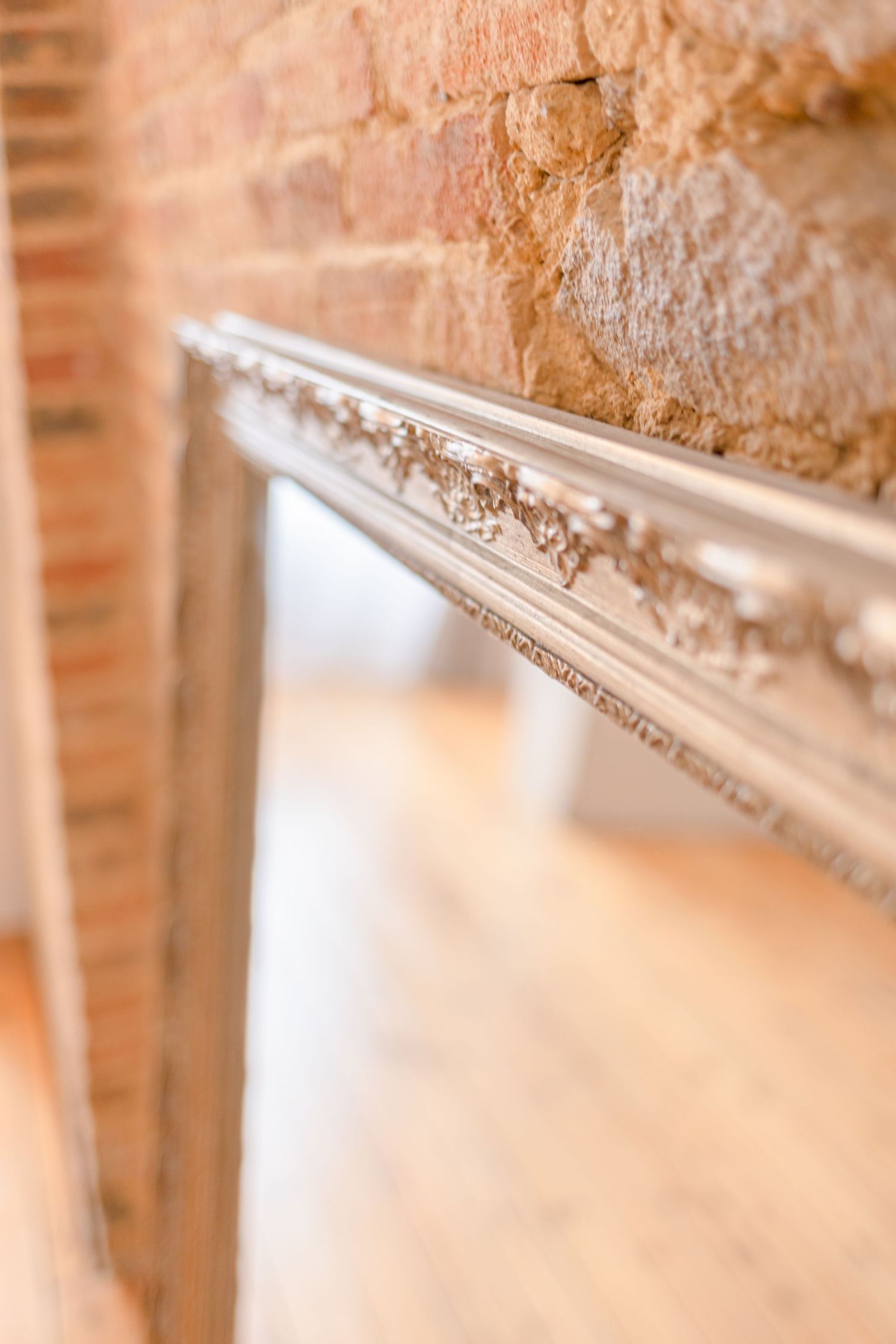 Detail of an ornate gilded picture frame against a rustic brick wall.