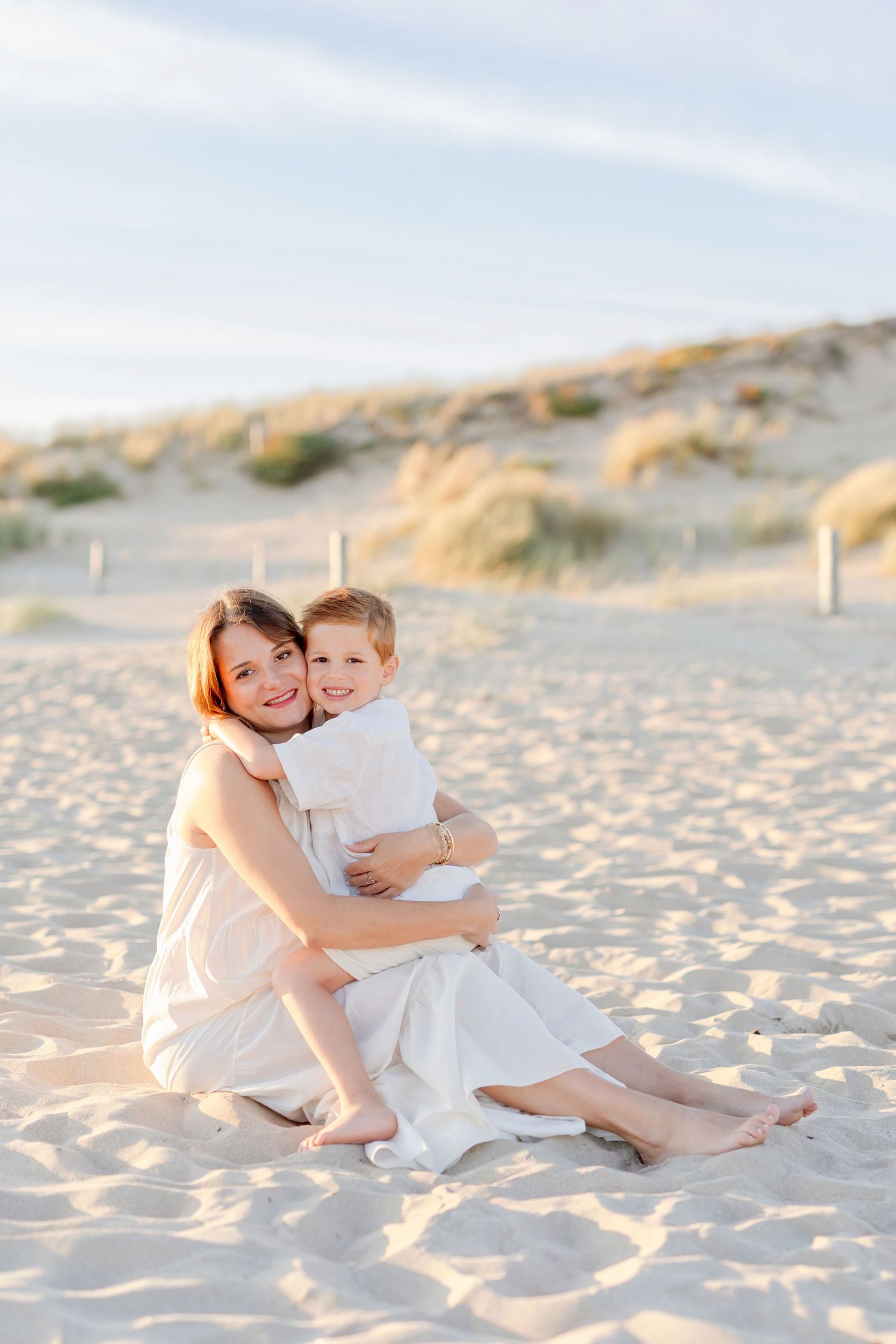 A tender moment shared between two people sitting on sandy beach at sunset.