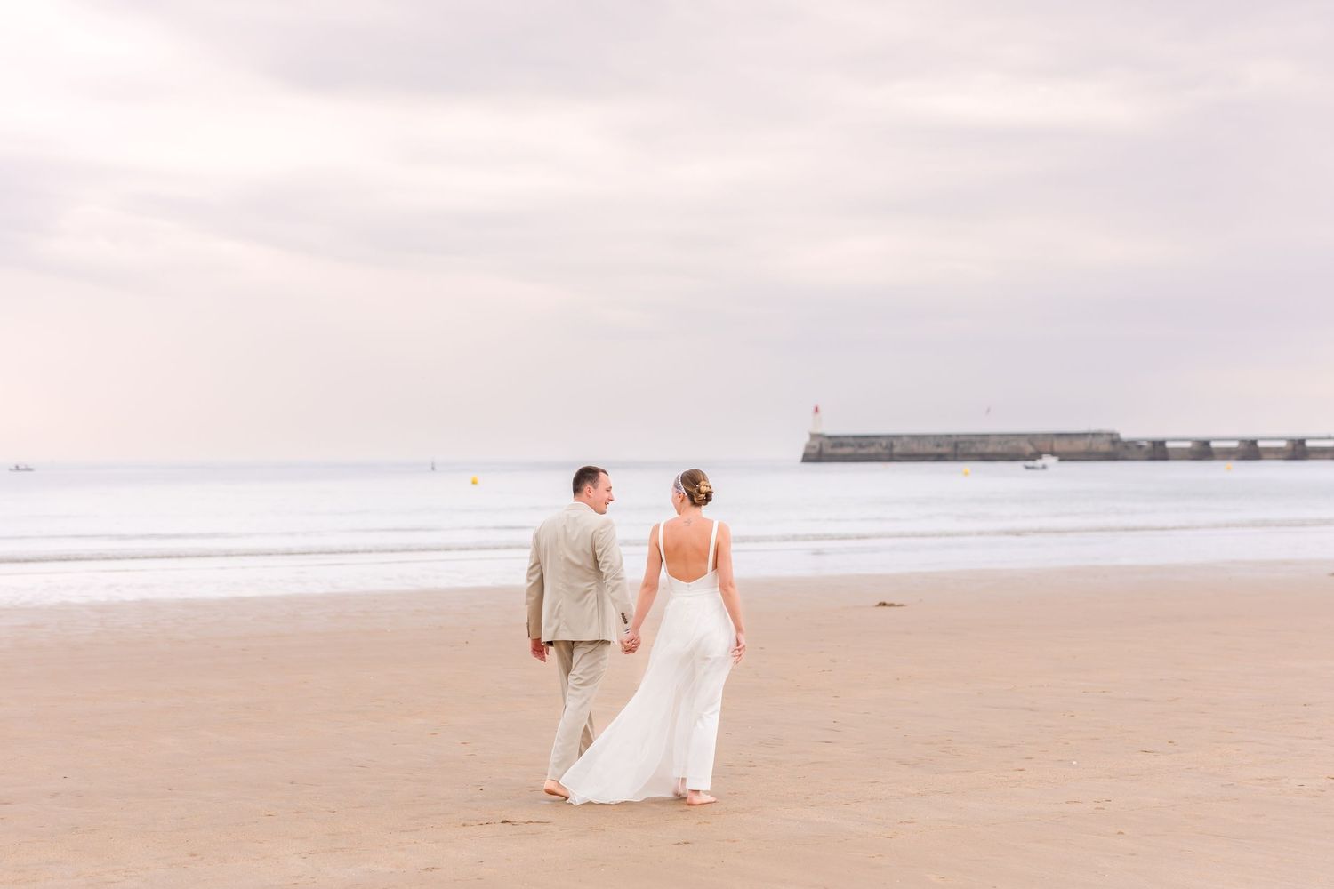 Couple walking along empty beach at sunset in wedding attire.