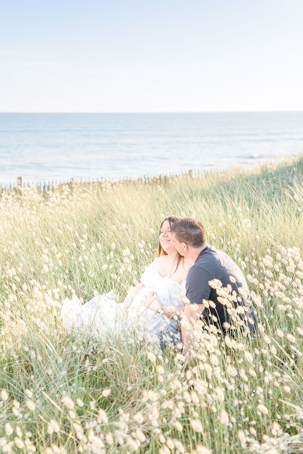 Two people share an intimate moment in a coastal meadow filled with white flowers.