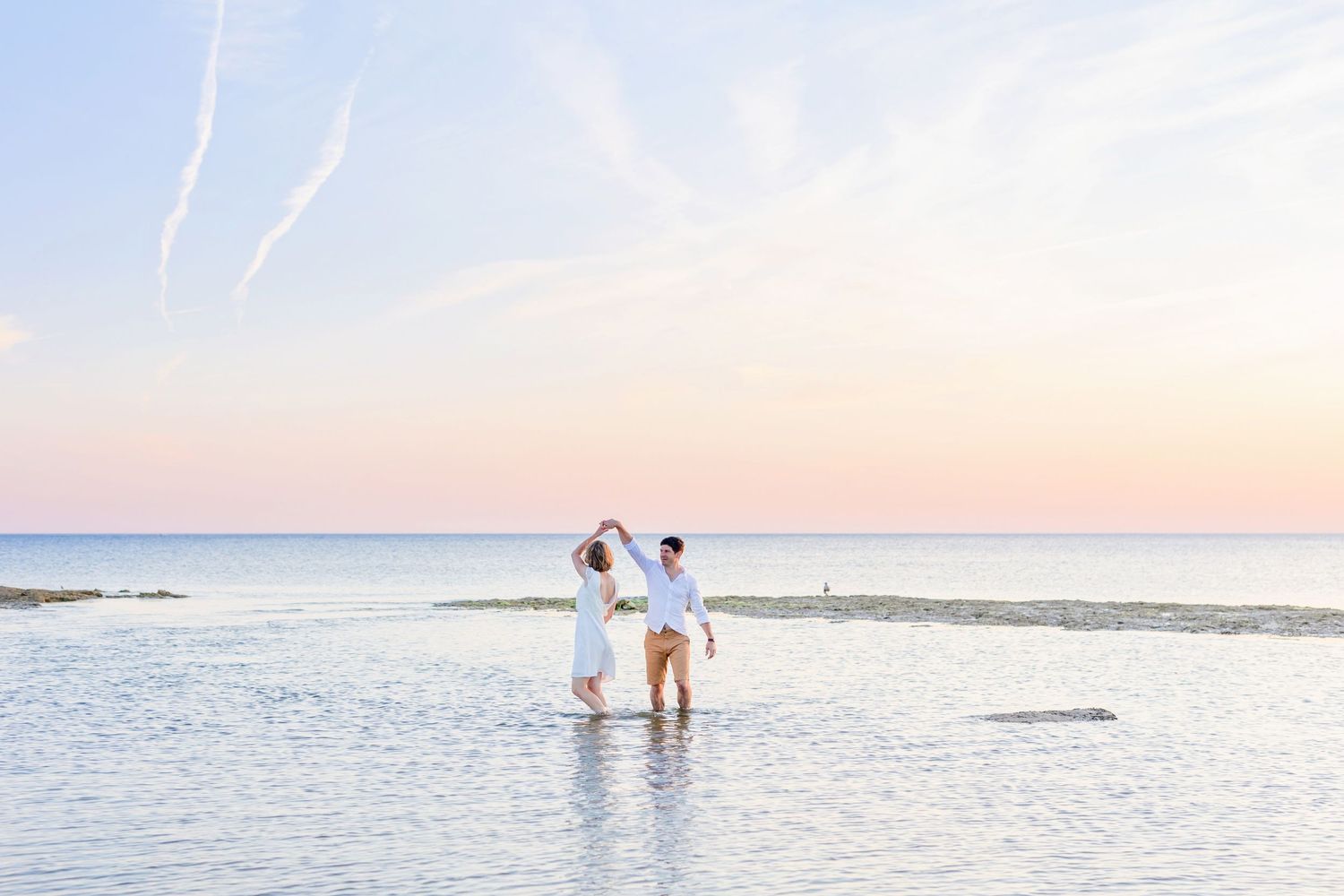 A tender moment between a couple wading in tranquil ocean waters at dusk.