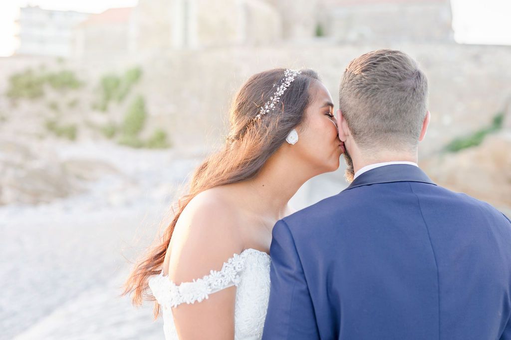 A romantic wedding moment captured on a rocky beach shore at sunset with soft pastel tones.