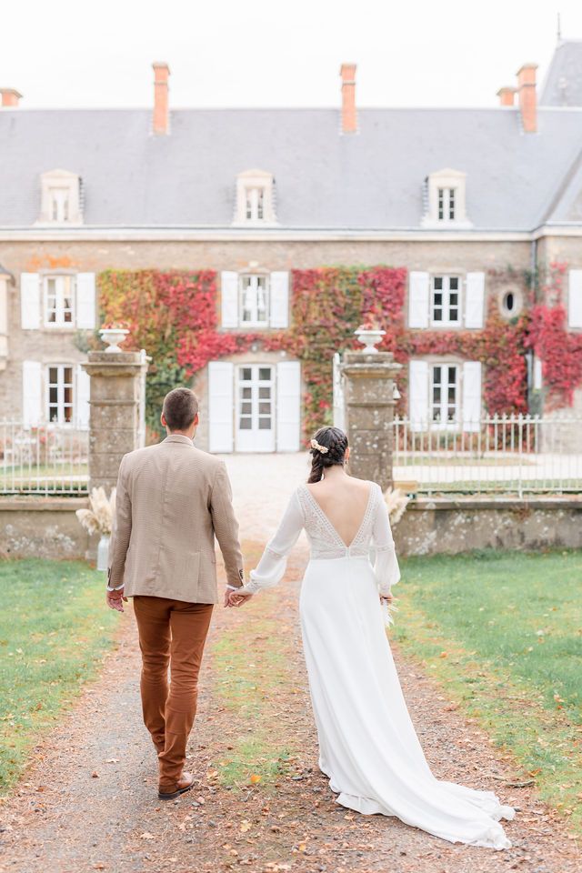Bride and groom walking away on gravel path toward ivy-covered chateau.