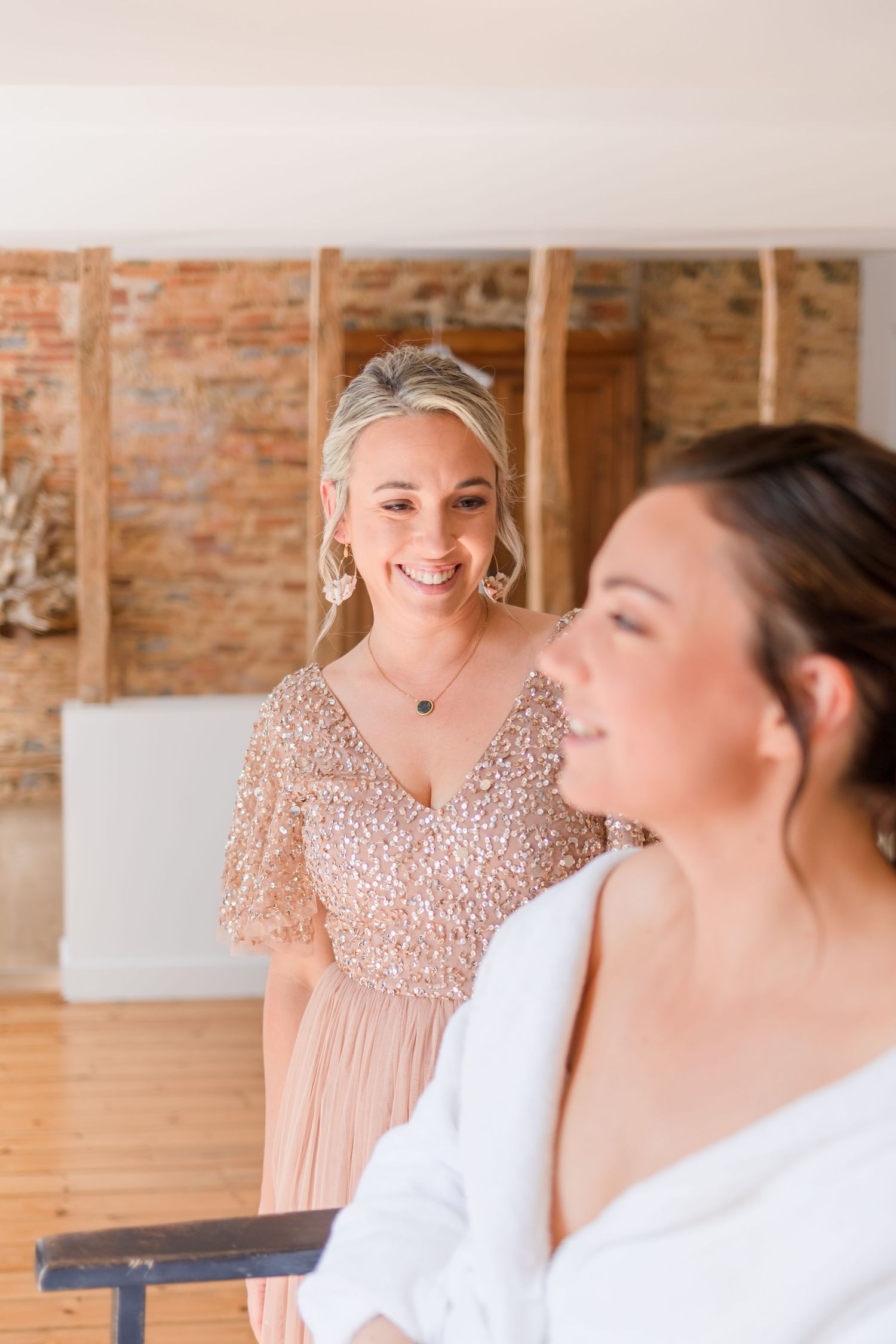 Wedding preparation scene in rustic brick-walled room with sparkly dress detail.
