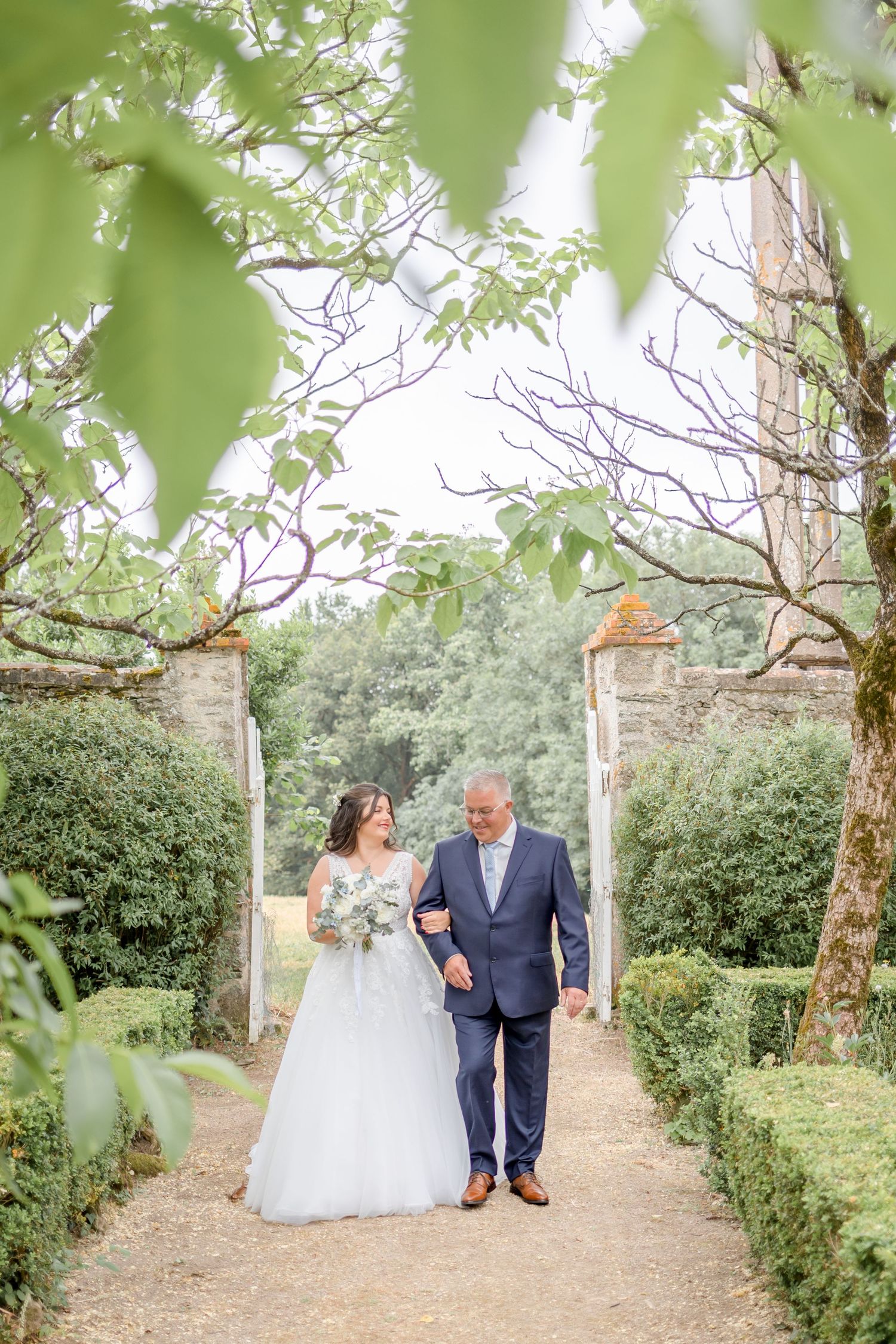 Garden pathway lined with trees and hedges on the grounds of an elegant estate.