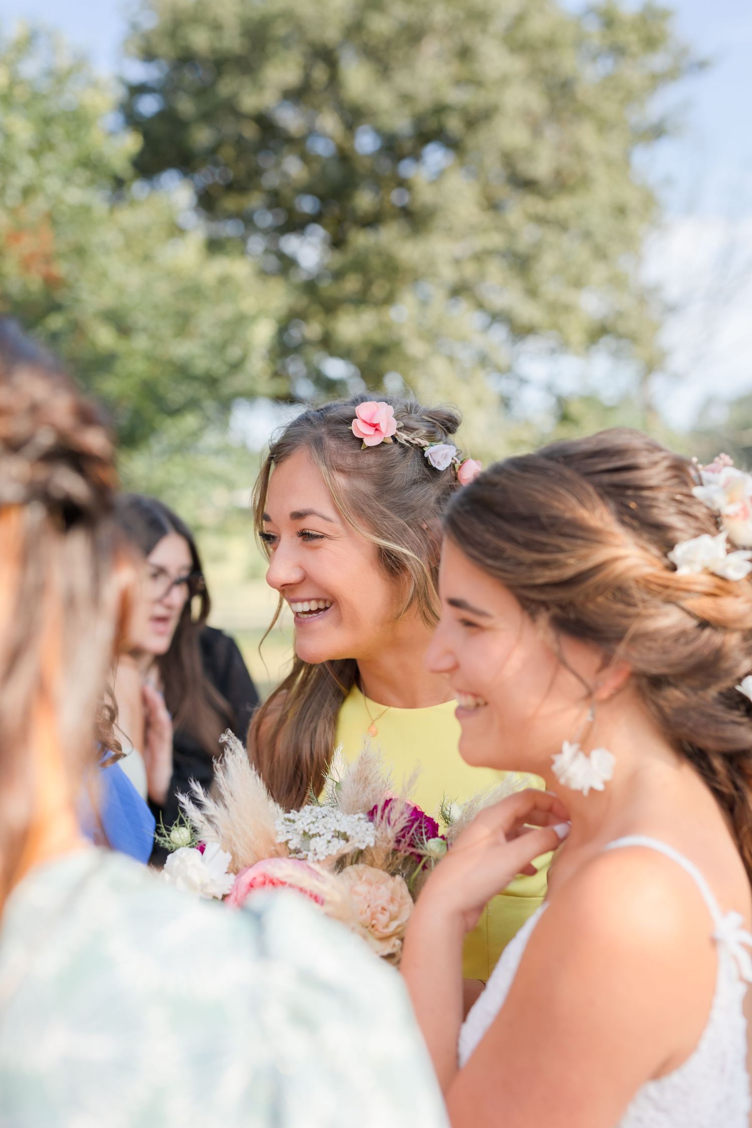 Wedding party members wearing floral headpieces share joyful laughter outdoors.