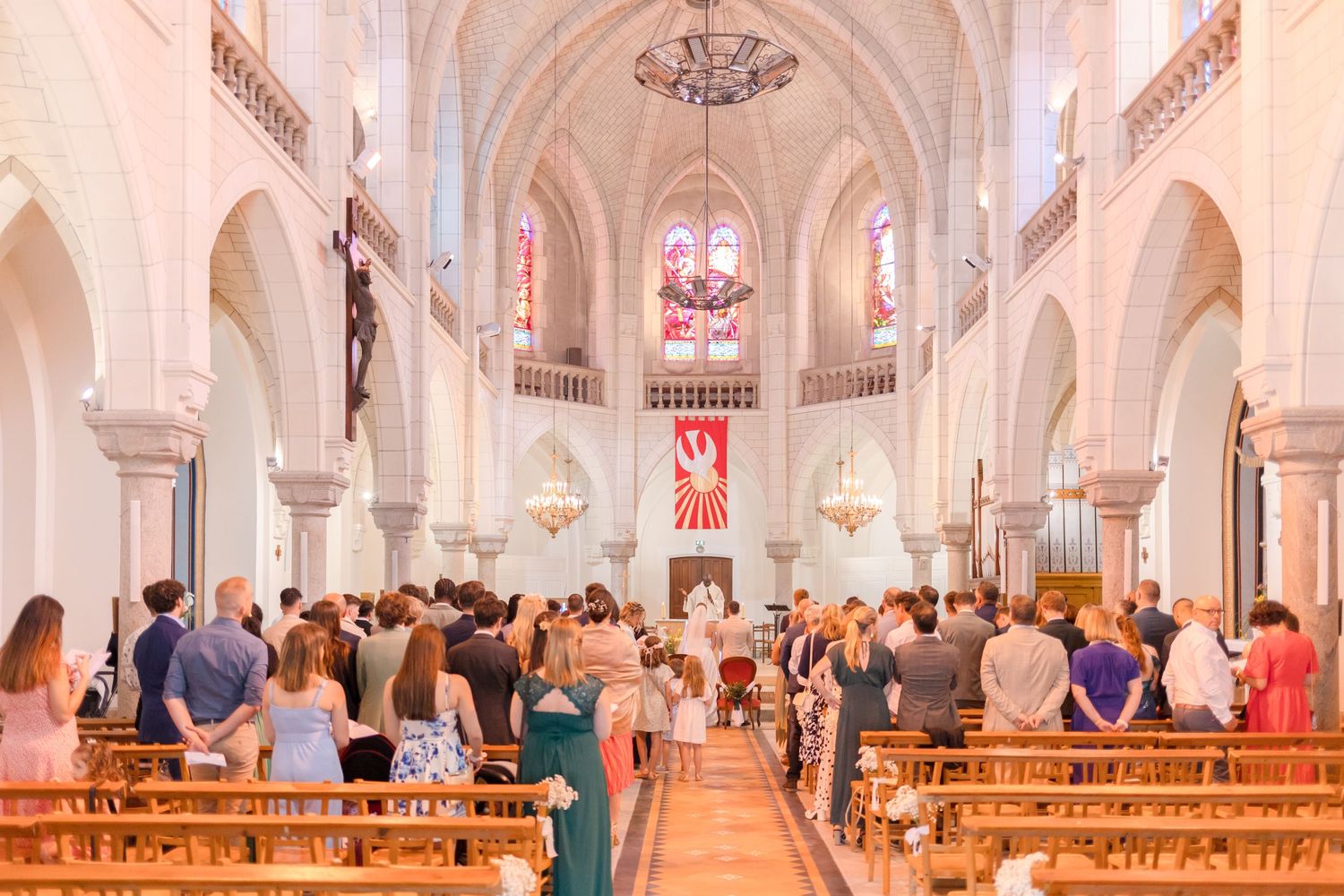 Interior of a grand cathedral during a wedding ceremony with vaulted ceilings and stained glass windows.