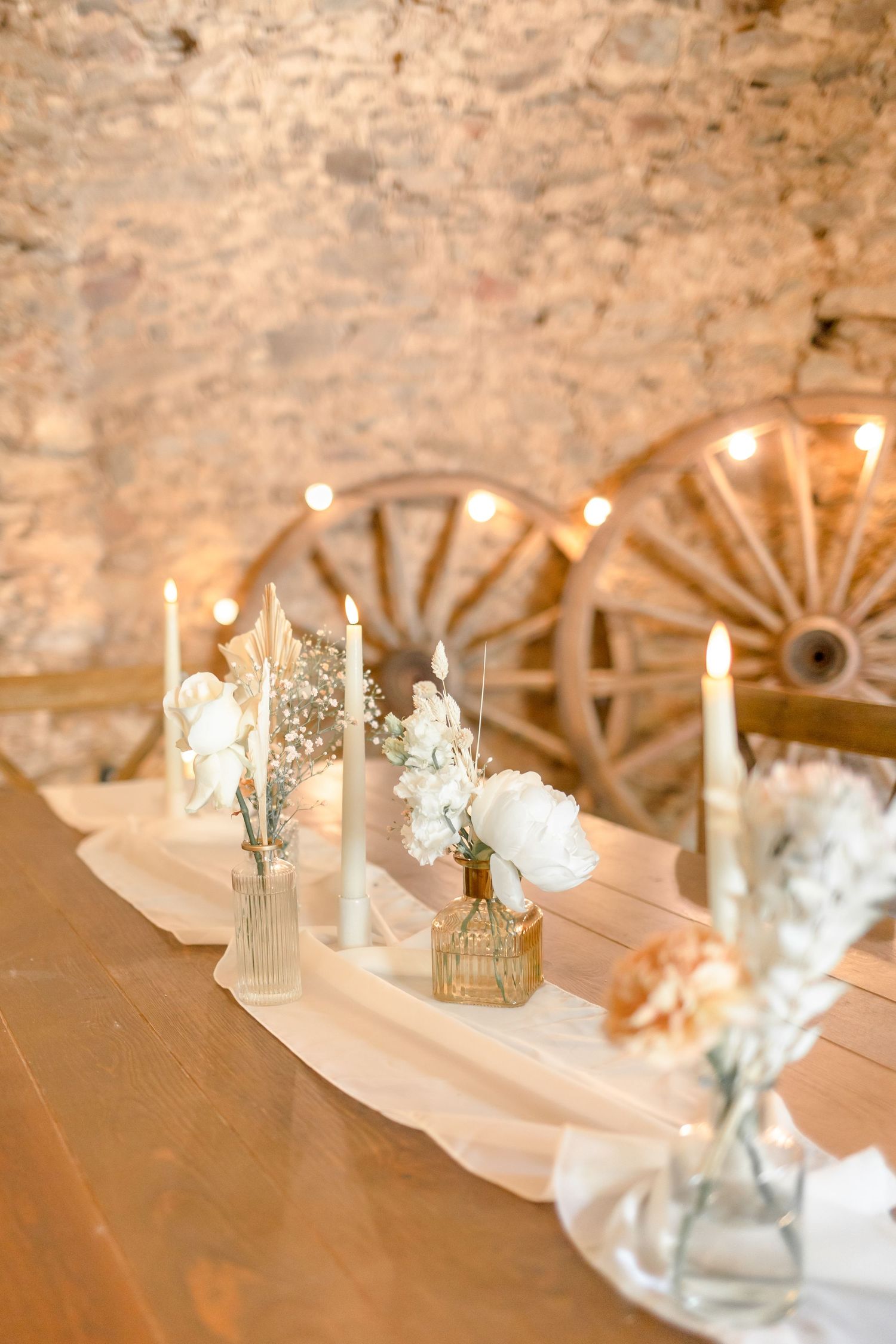 Elegant table setting with delicate candles and floral arrangements against rustic wagon wheel decor.
