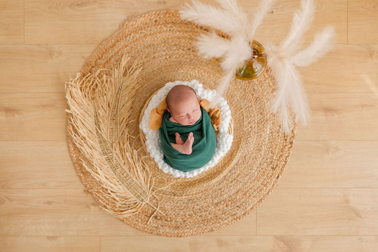 Bird's eye view of sleeping baby in green wrap centered in circular woven mat with white accents.