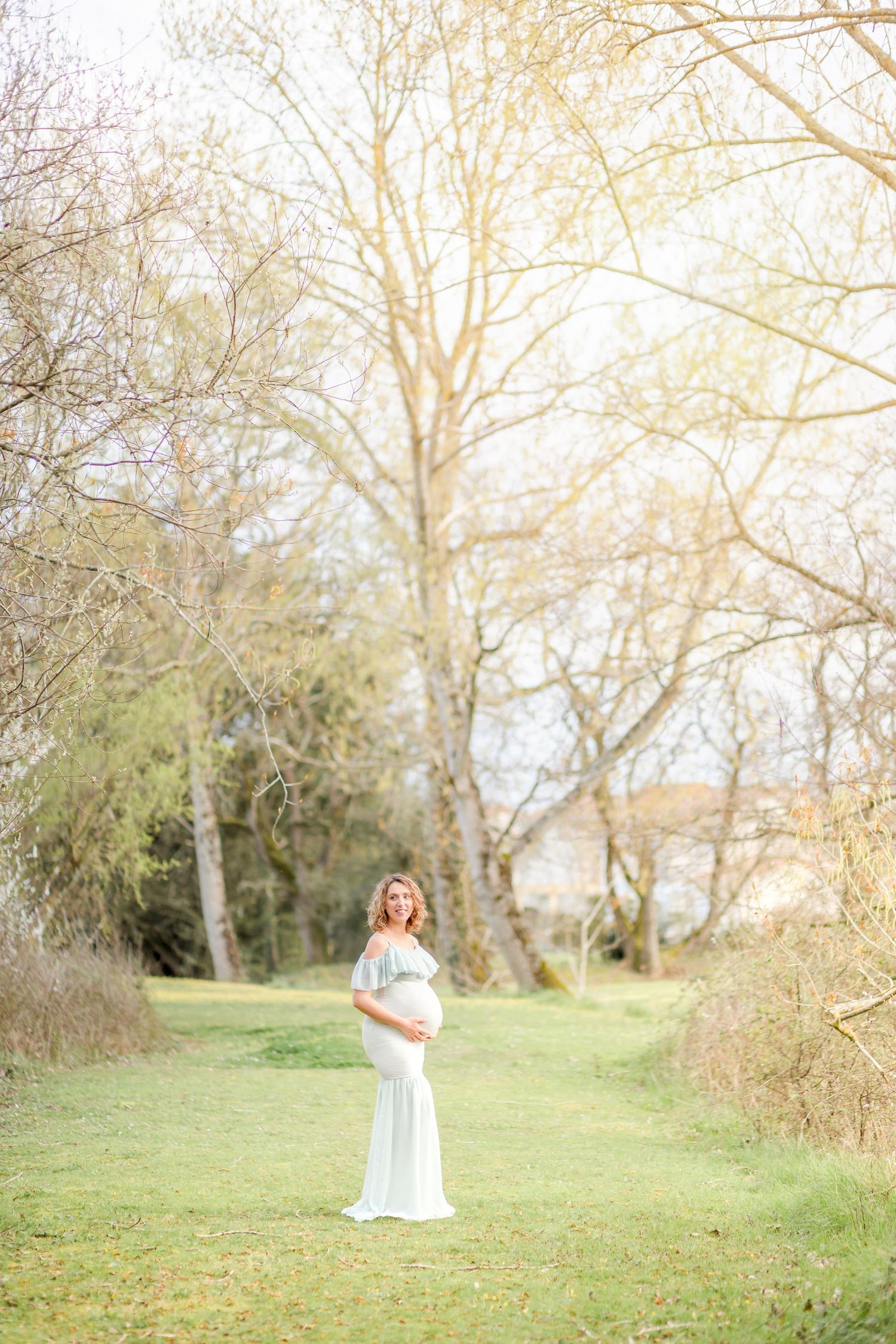 Maternity photo in a dreamy woodland setting with soft natural light filtering through trees.