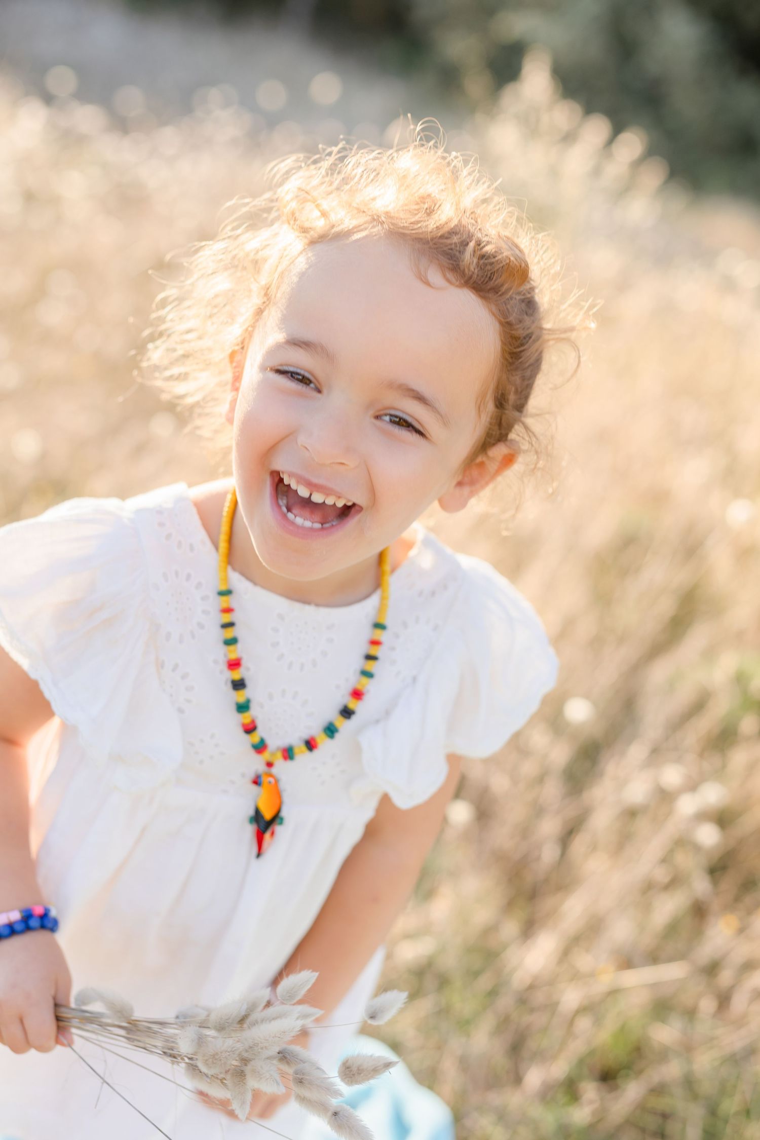 Laughing child wearing colorful necklace in sunlit summer field.
