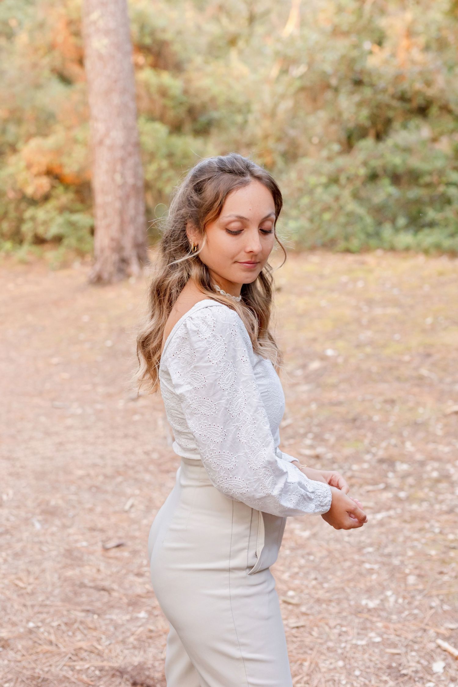 Person in white outfit poses elegantly on autumn forest path.