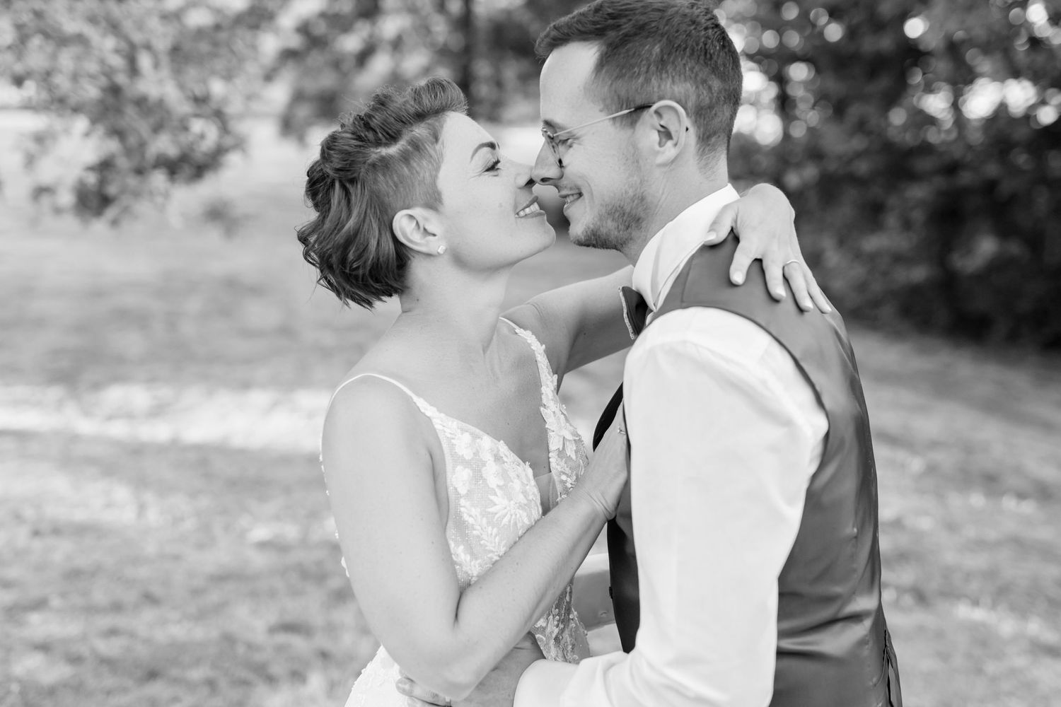 A romantic black and white wedding photo showing a tender moment between newlyweds in an outdoor setting.
