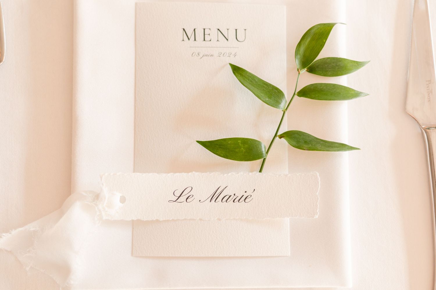 Close-up of wedding menu card with fresh green leaves on crisp white linens.