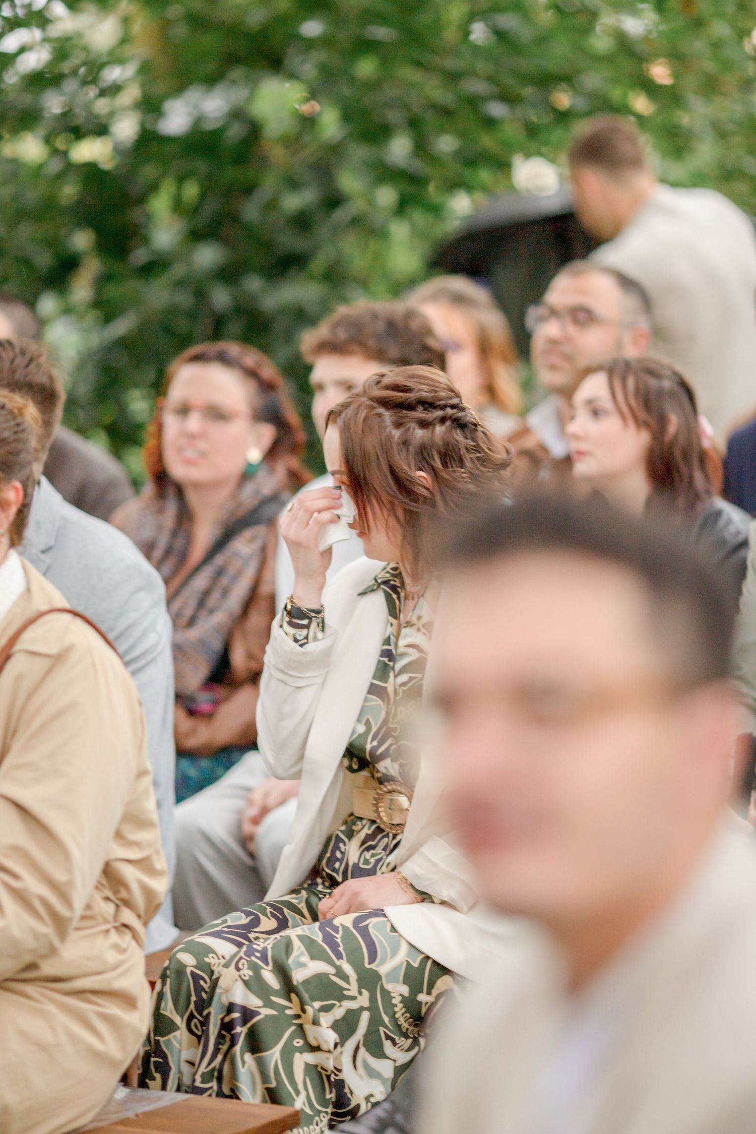 Wedding guests seated on wooden benches during outdoor forest ceremony.