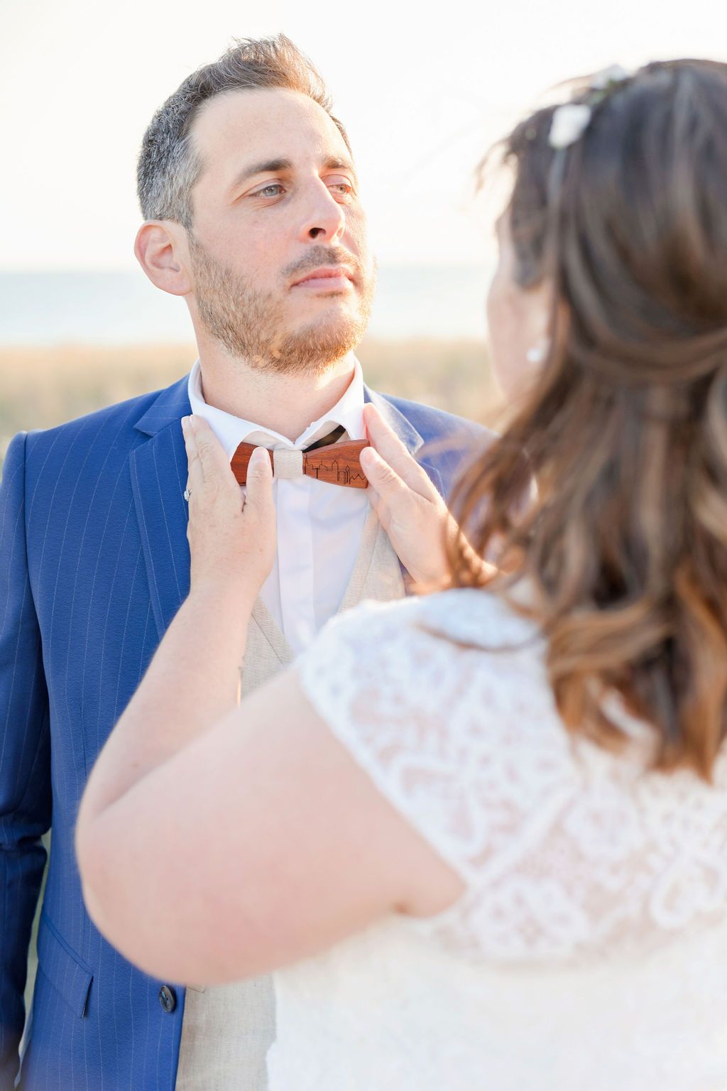 An intimate wedding moment with formal attire adjustments against an ocean backdrop.