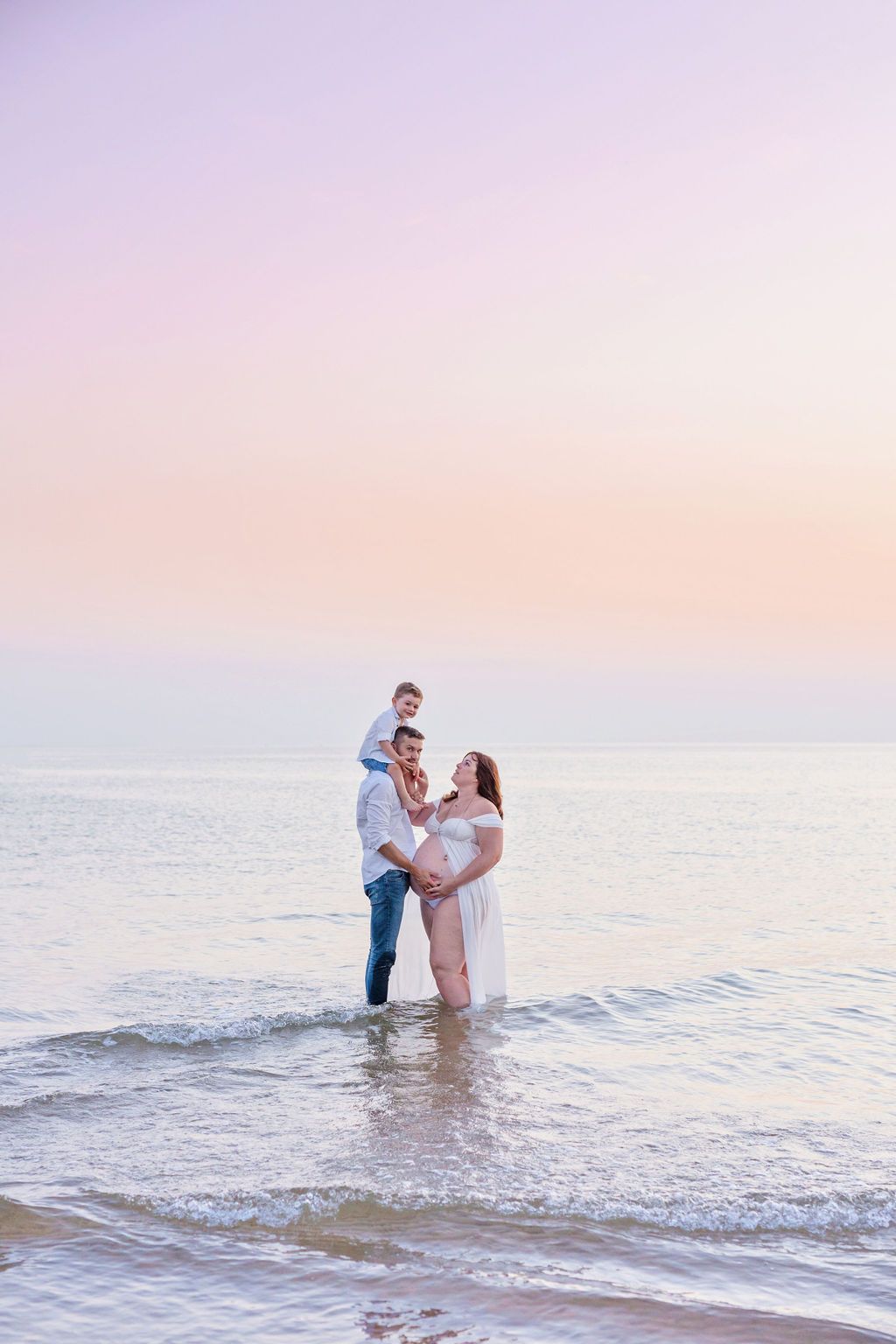 Expectant couple sharing intimate moment during beach maternity photoshoot at dusk.