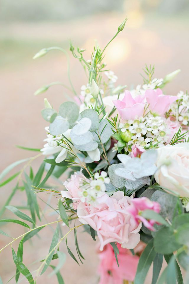 Delicate pink and white wedding bouquet with roses and greenery in soft pastel tones against blurred background.