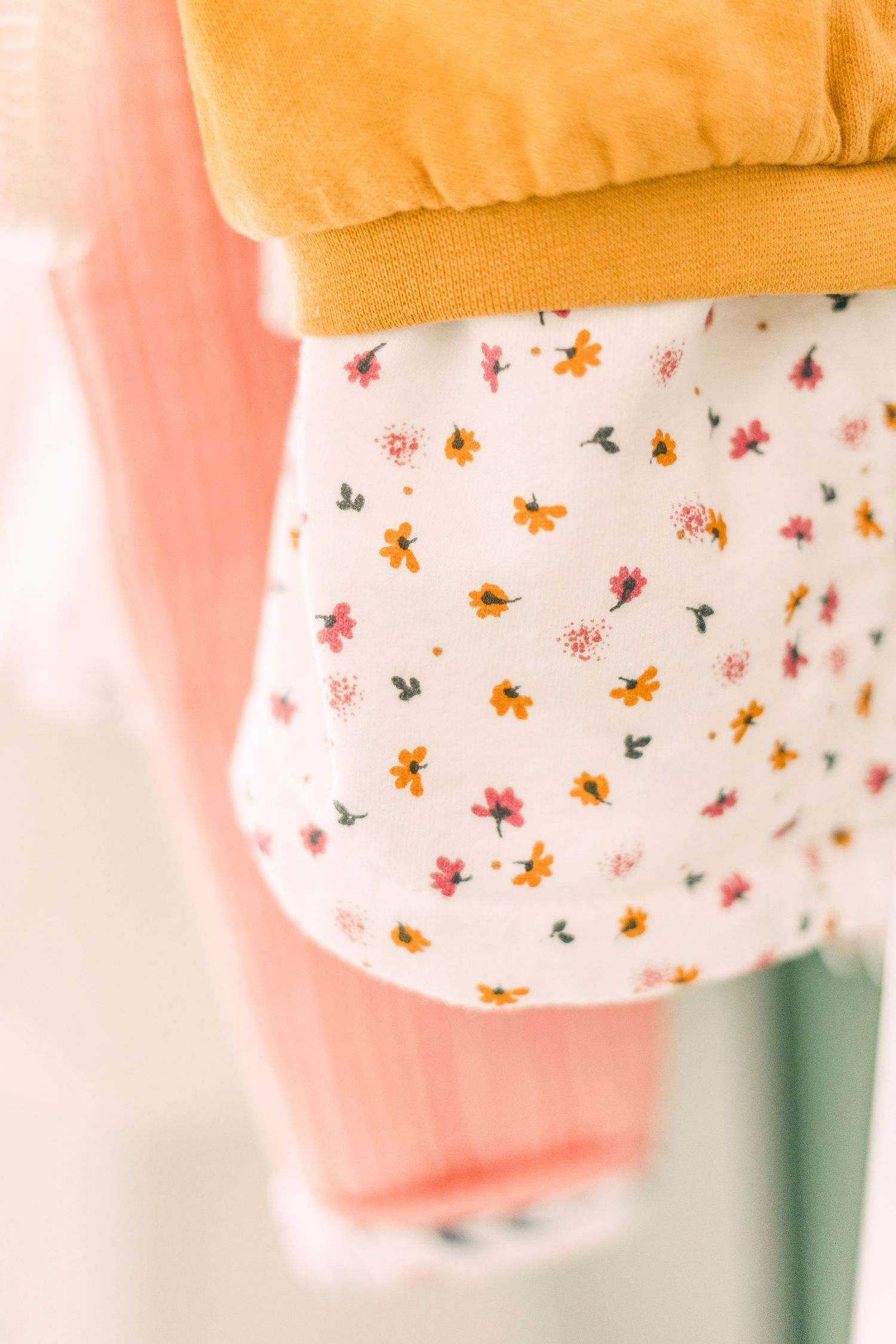 Close-up of a white fabric with delicate pink and orange floral pattern against a peachy background.