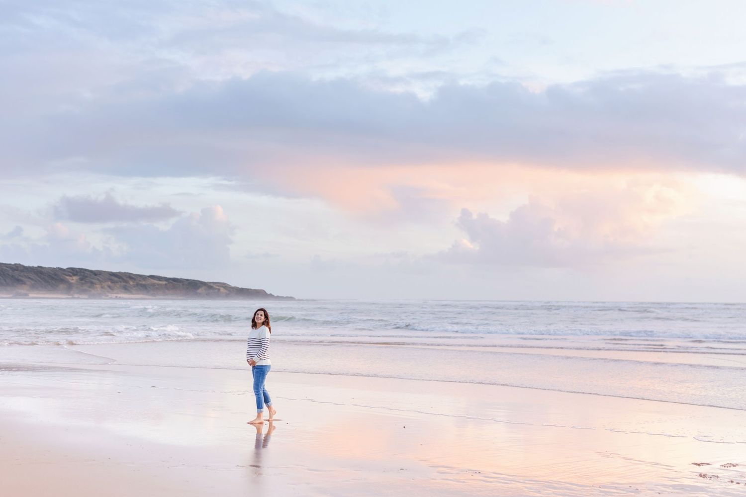 A lone figure stands on a beach during a pink and purple sunset.
