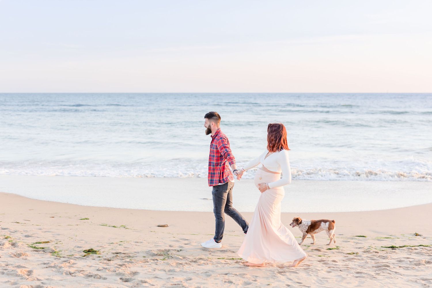Family walking along ocean shoreline with their dog during sunset.