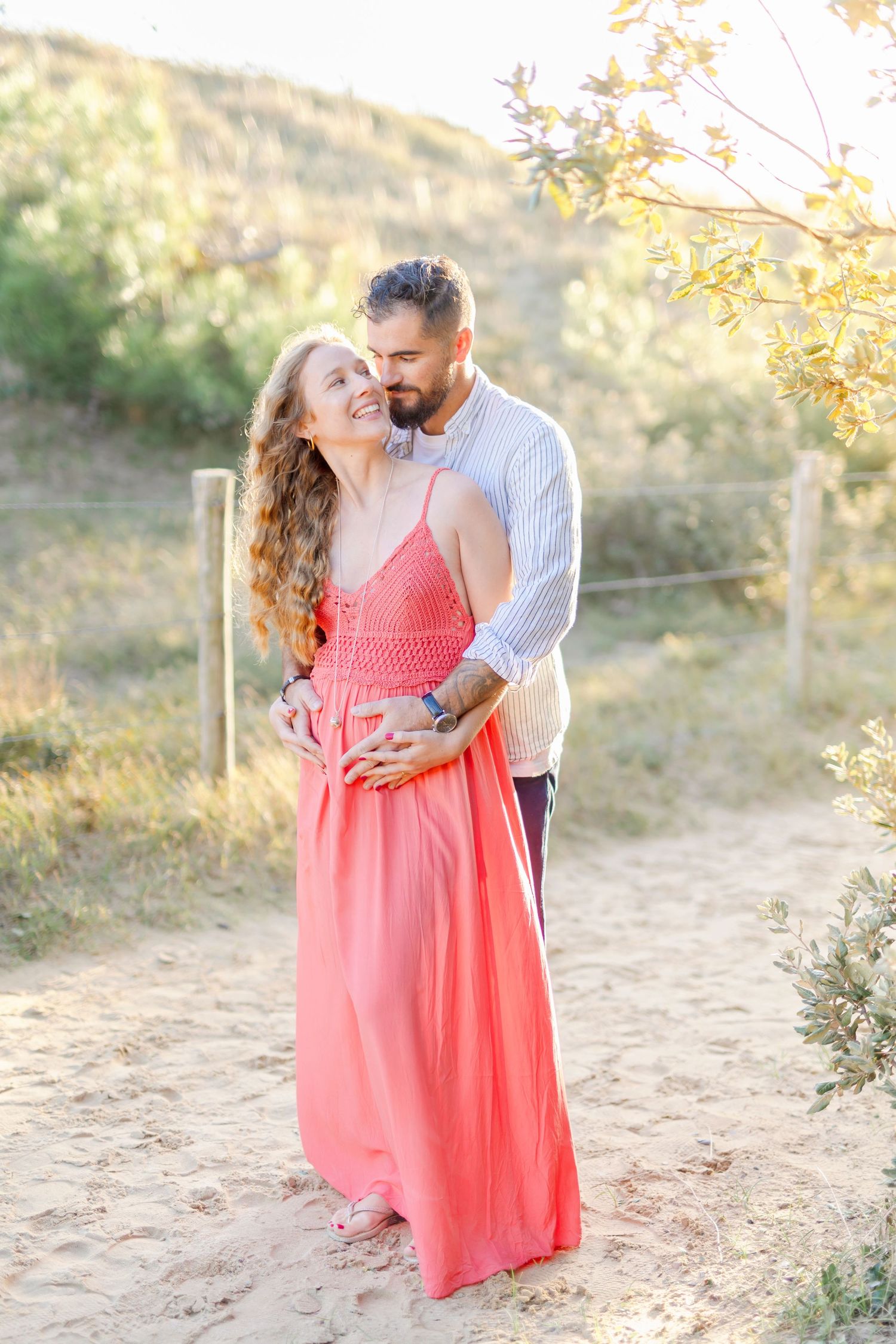 Couple embracing outdoors in a natural setting with coral dress and striped shirt.