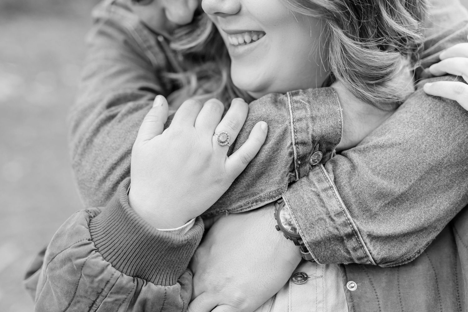 Close-up black and white photo showing gentle embrace and engagement ring.