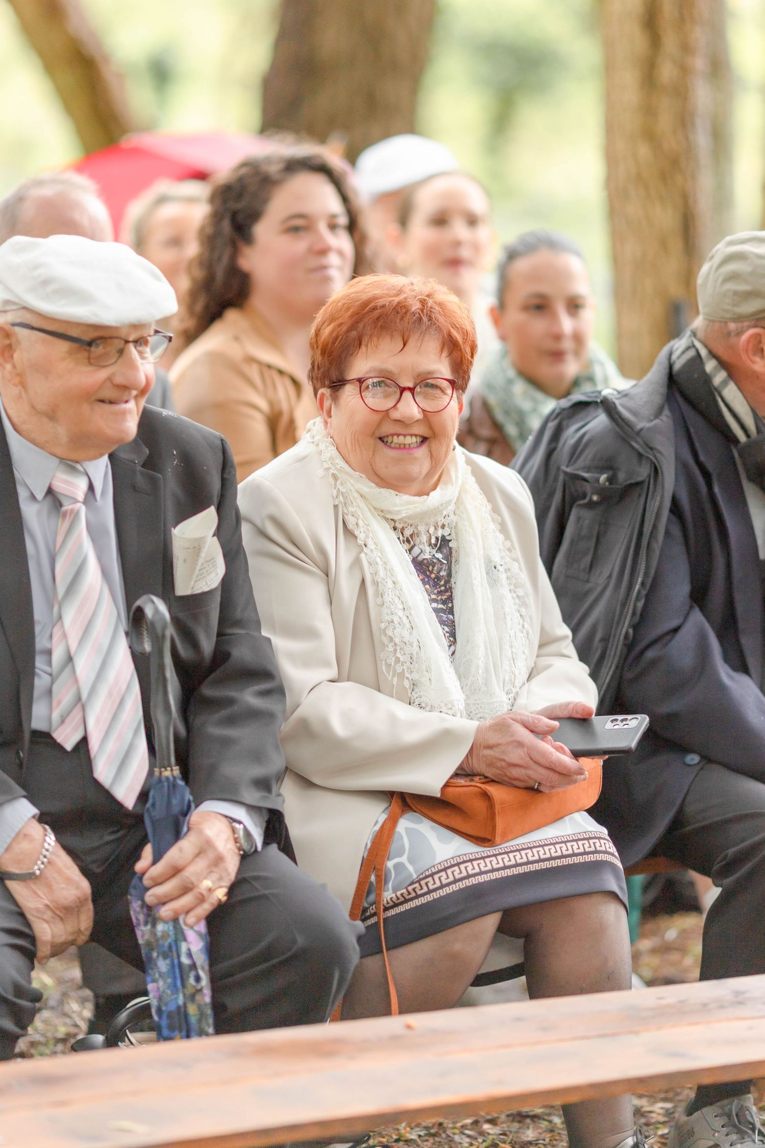 Wedding guests seated on wooden benches at an outdoor ceremony.