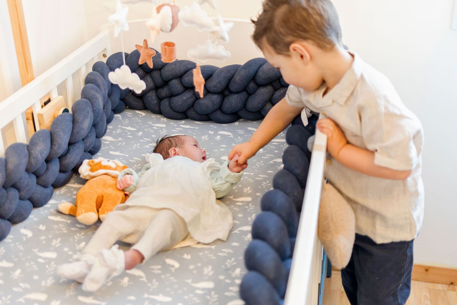 Nursery scene with braided navy bumper and orange toy, showing interaction with infant.