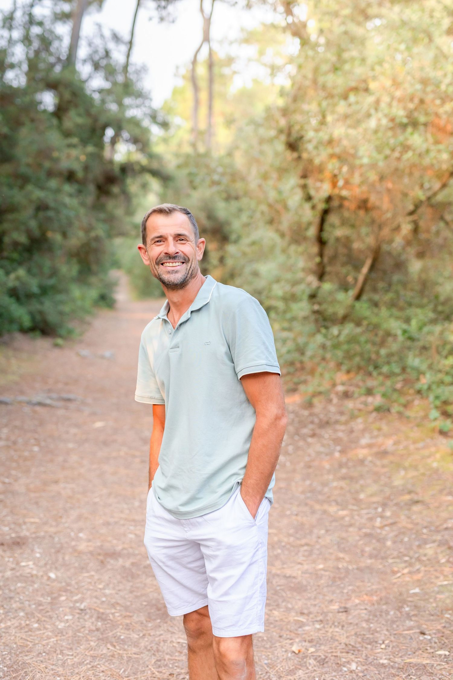 A person in a light blue shirt and white shorts stands on a nature trail in warm sunlight.