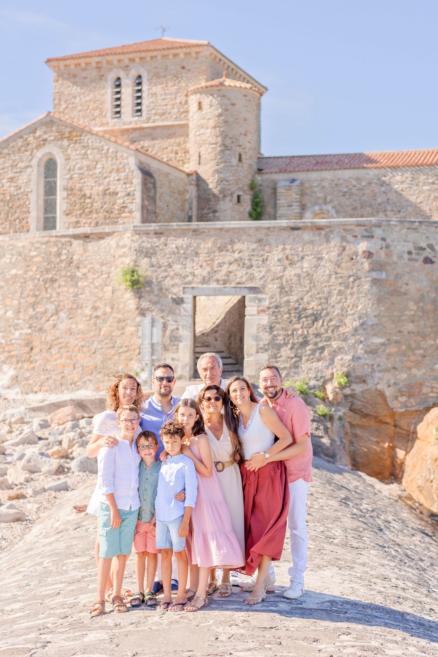 Family group photo in front of historic stone church building on Mediterranean coast.