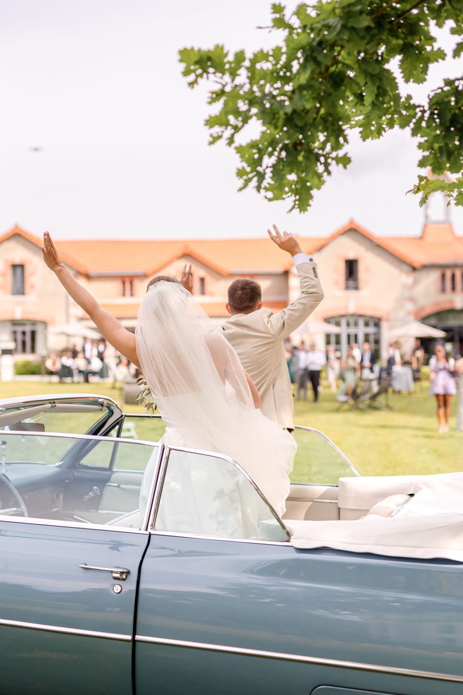 Wedding couple celebrating in vintage convertible car with arms raised in joy.