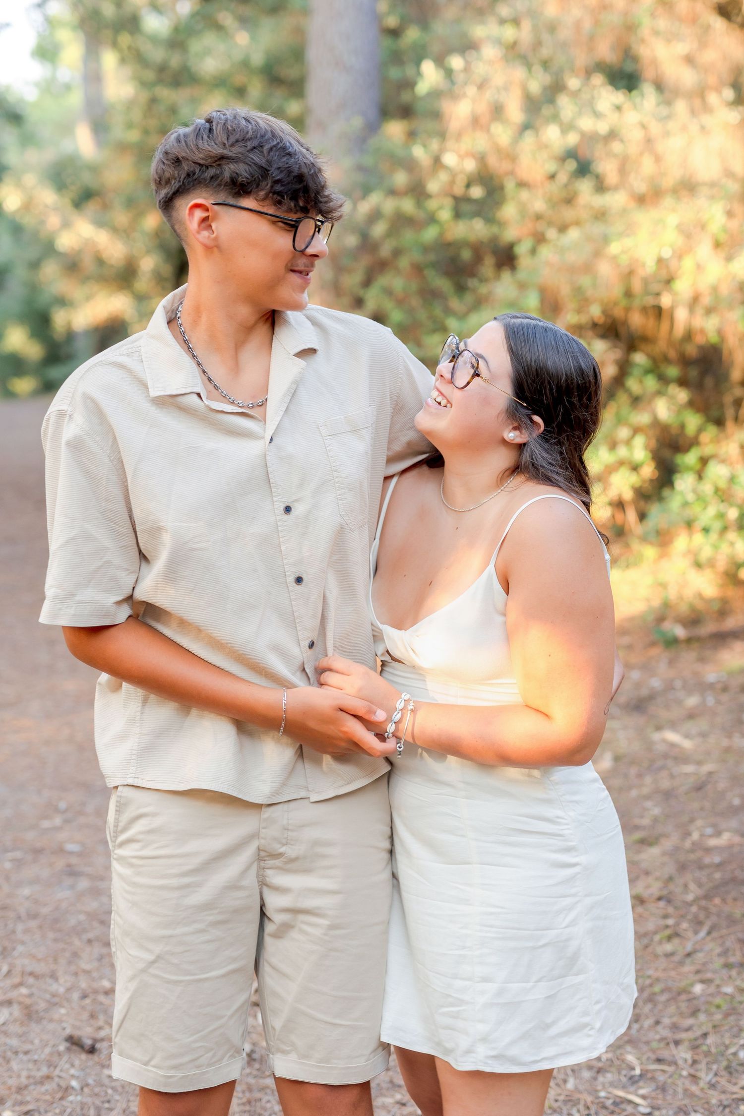 A couple in matching light colored outfits sharing a tender moment on a forest path.
