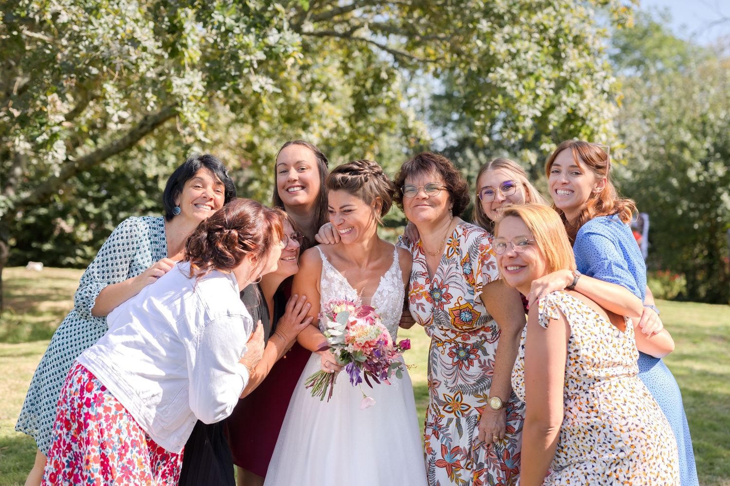 Joyful wedding party gathering outdoors sharing laughter and smiles on a sunny day.