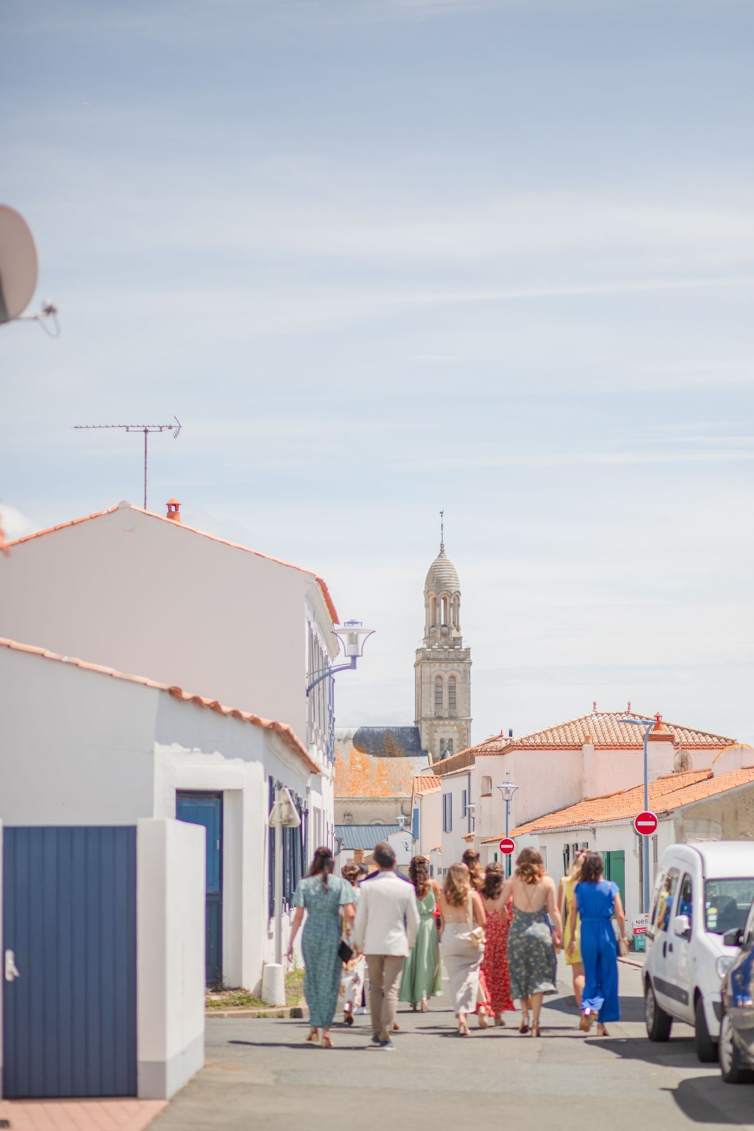 People walking through quaint village streets with white buildings and terracotta roofs.