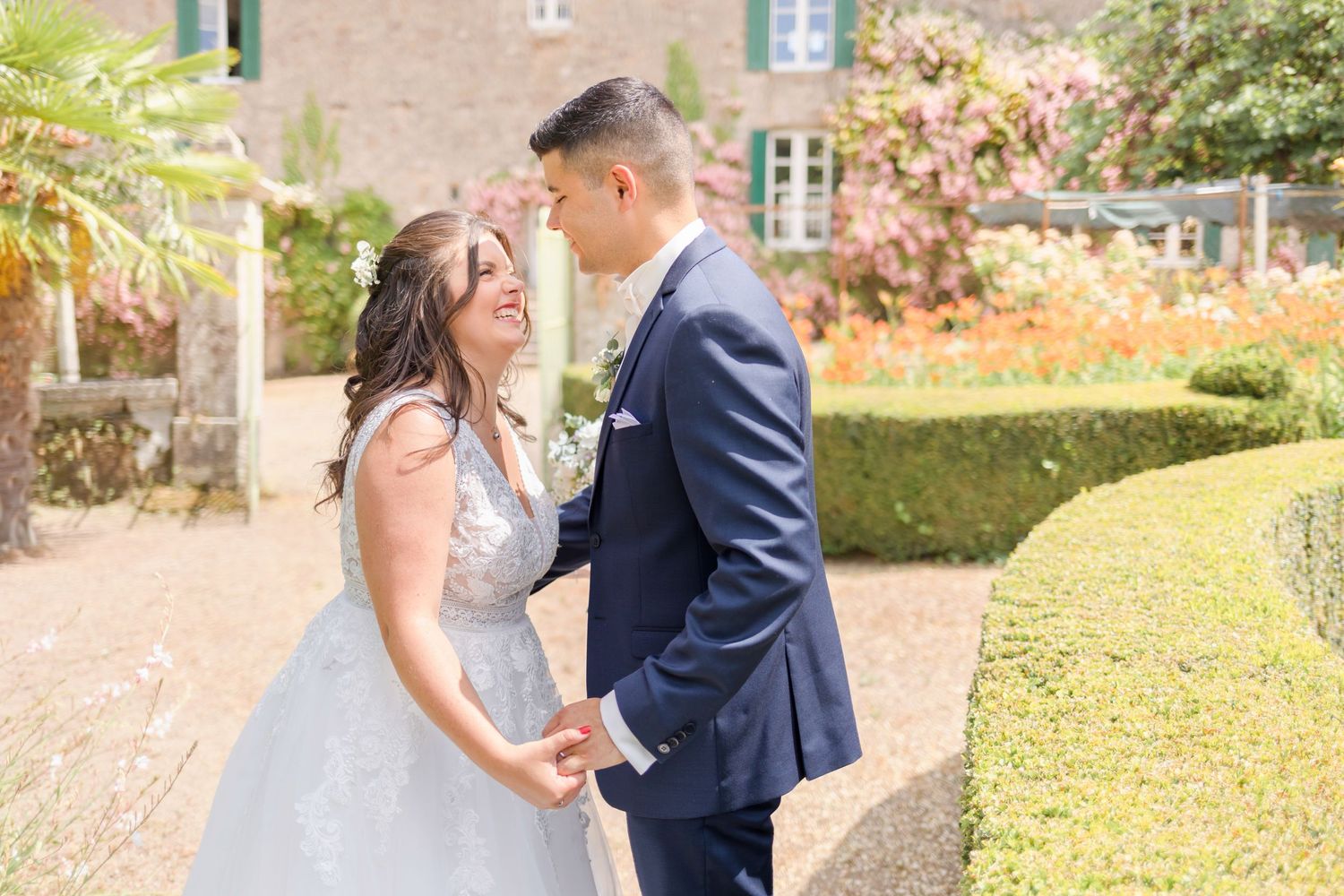 A tender moment between newlyweds in a sunlit garden with manicured hedges and stone architecture.