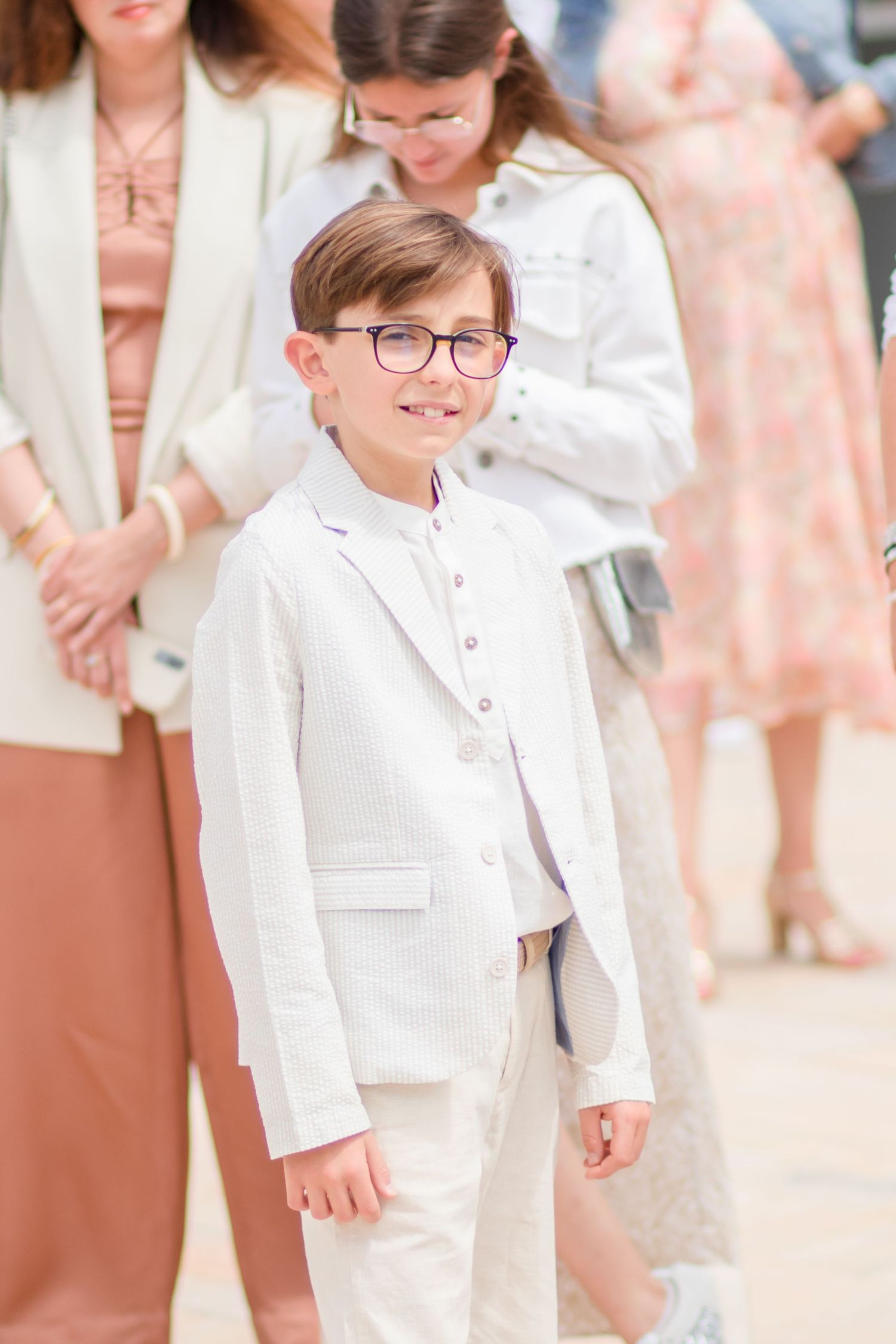 A young ring bearer in a white suit smiles during a wedding ceremony.