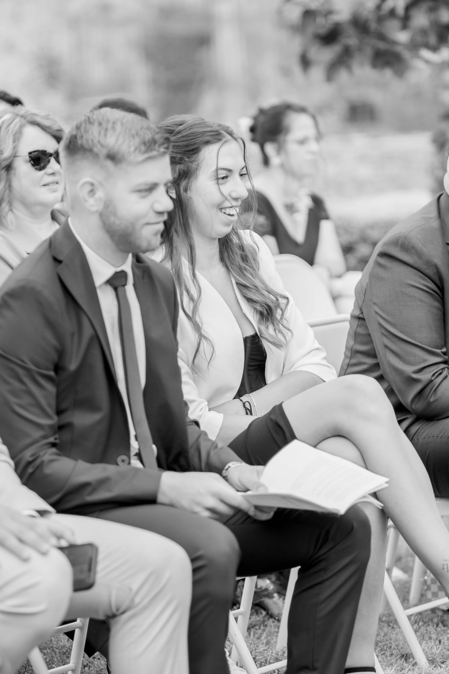 Wedding guests seated in white chairs during an outdoor ceremony.