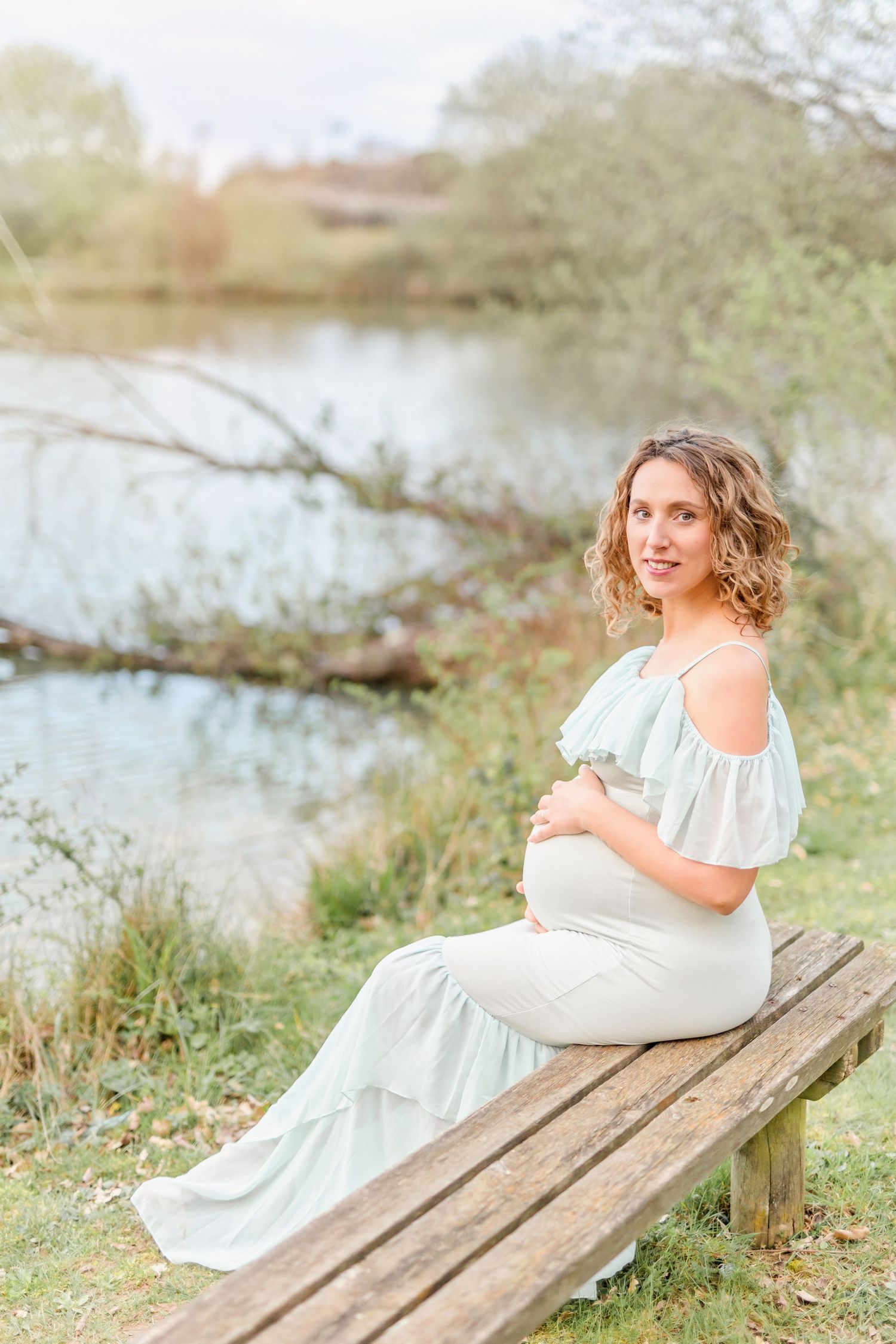 Elegant maternity photos captured on a wooden bench beside a tranquil lake.