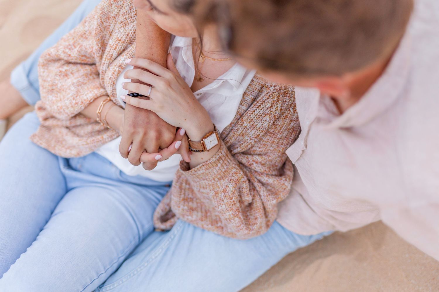 Close up of hands clasped together while sitting on sandy beach.