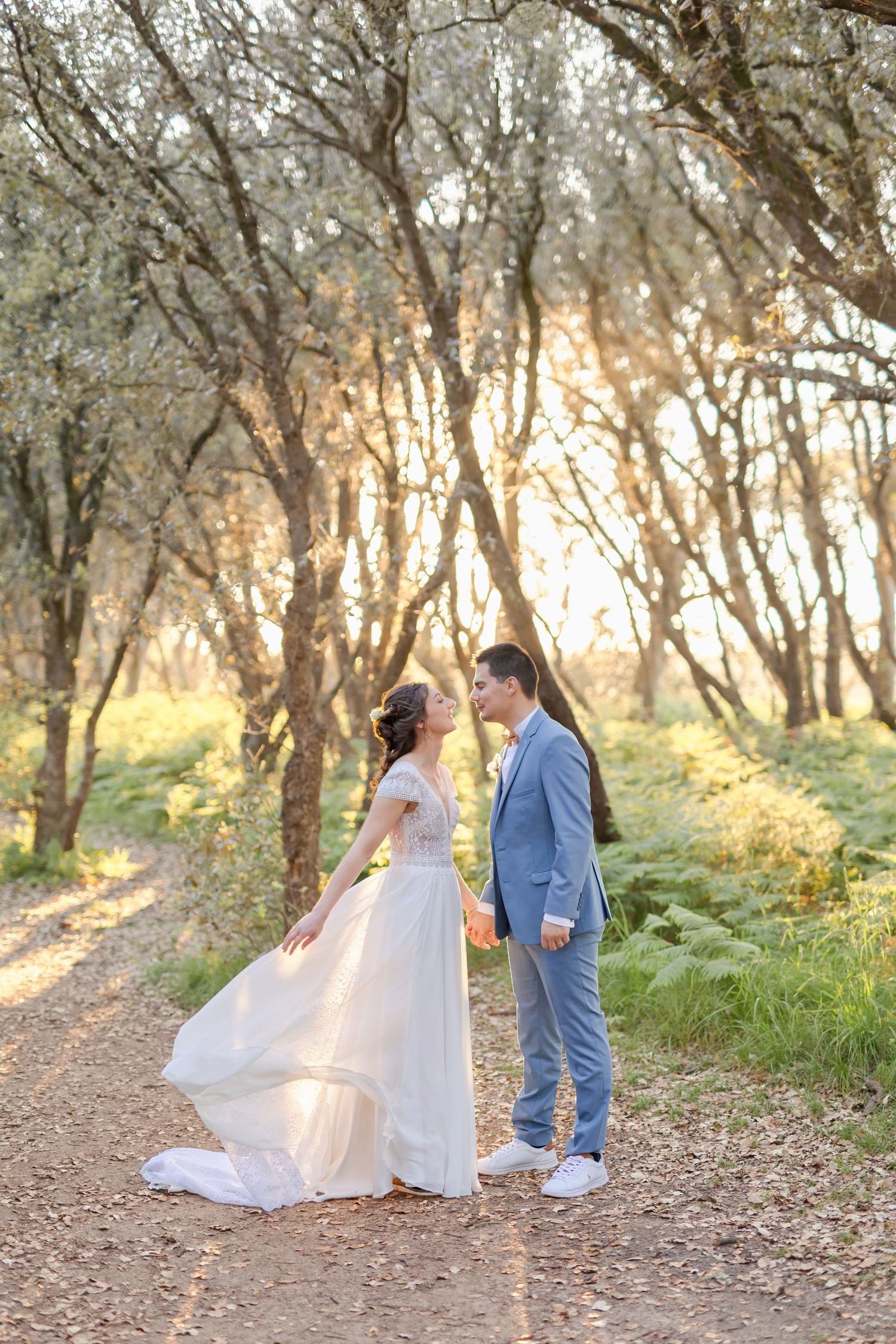 Romantic wedding photo on a forest trail with flowing white dress and light blue suit.